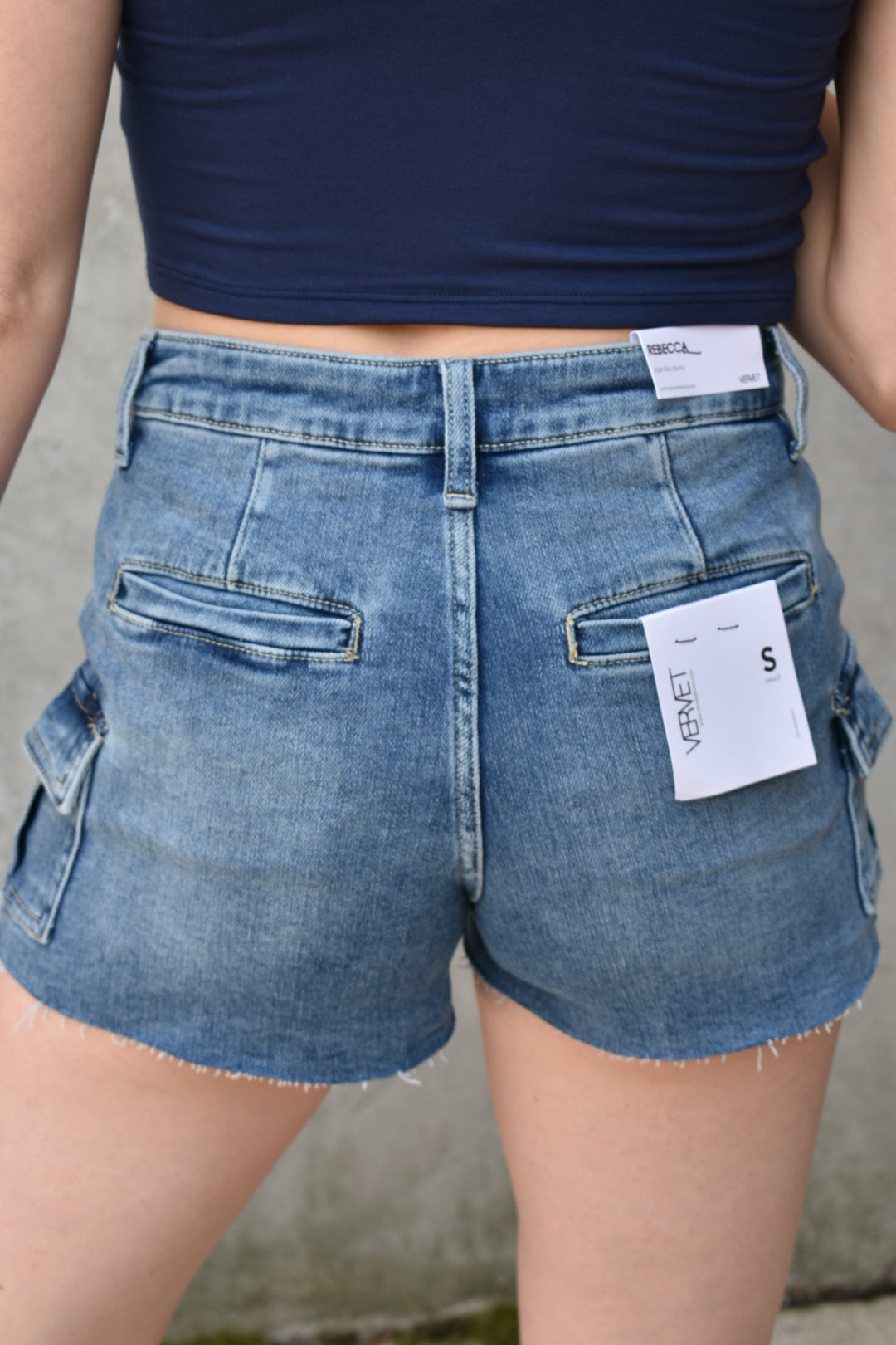 denim high rise medium wash cargo shorts with small cargo style pockets on the side. Stretch denim. The brand is Vervet