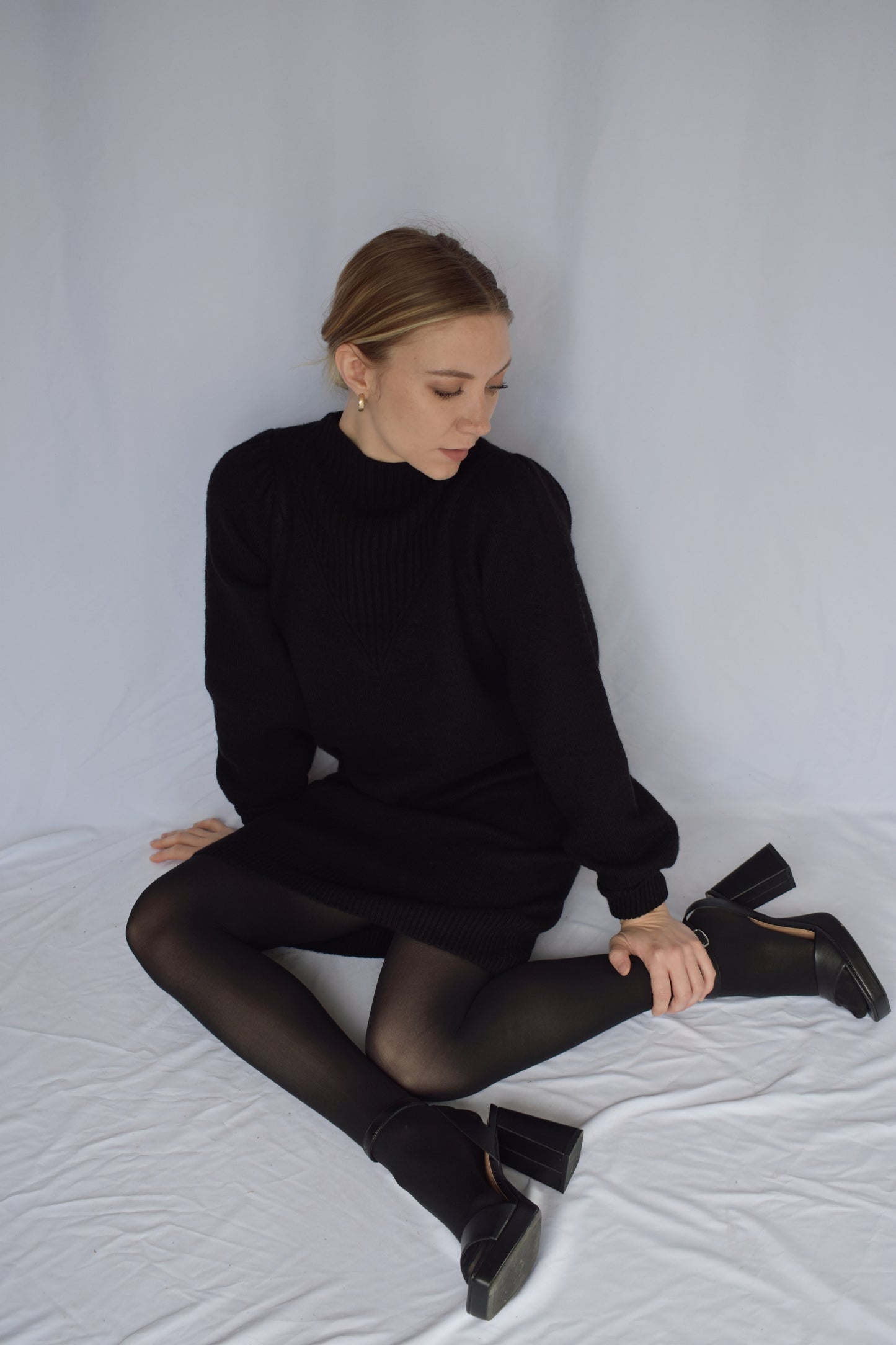 black sweater dress with long sleeves. ribbed cuffs and mock neck with v neck ribbed detail. slight puff on shoulders. hits just above the knees. relaxed fit, not oversized.