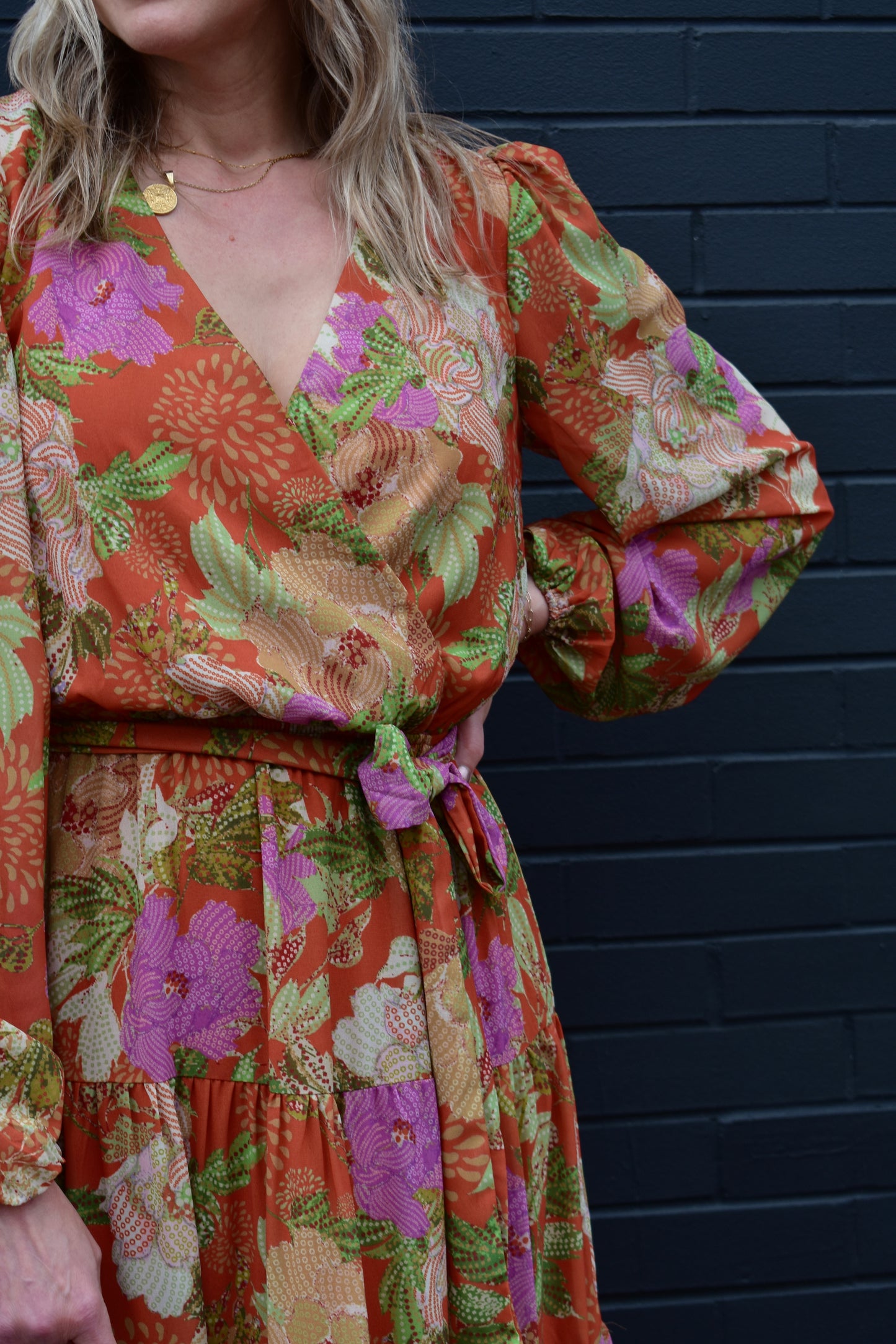 Long sleeve midi dress with floral print. Colors are an orange background with yellow, purple, light pink, green, white and cream. Wrap V neckline, lightweight fabric with lining, elastic at wrists, wrap at waist, tiered skirt.