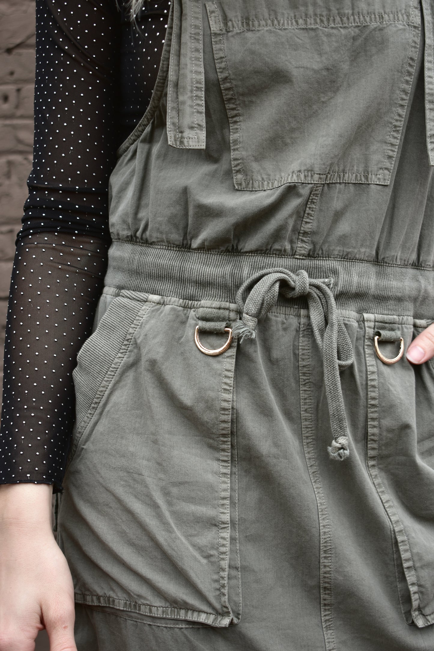 olive overall dress, midi length, adjustable straps, waist drawstring, front slit up skirt, front and back patch pockets, and a pocket on the front.