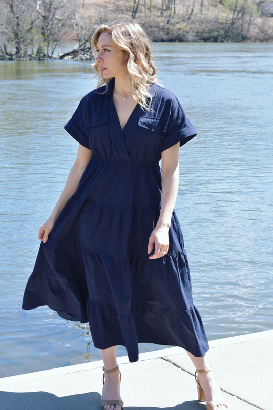 navy blue midi dress with tiered skirt and synched waist. drop shoulder cuffed short sleeves with v neck. collar and two flap enclosure faux breast pockets. has side pockets in skirt of dress.