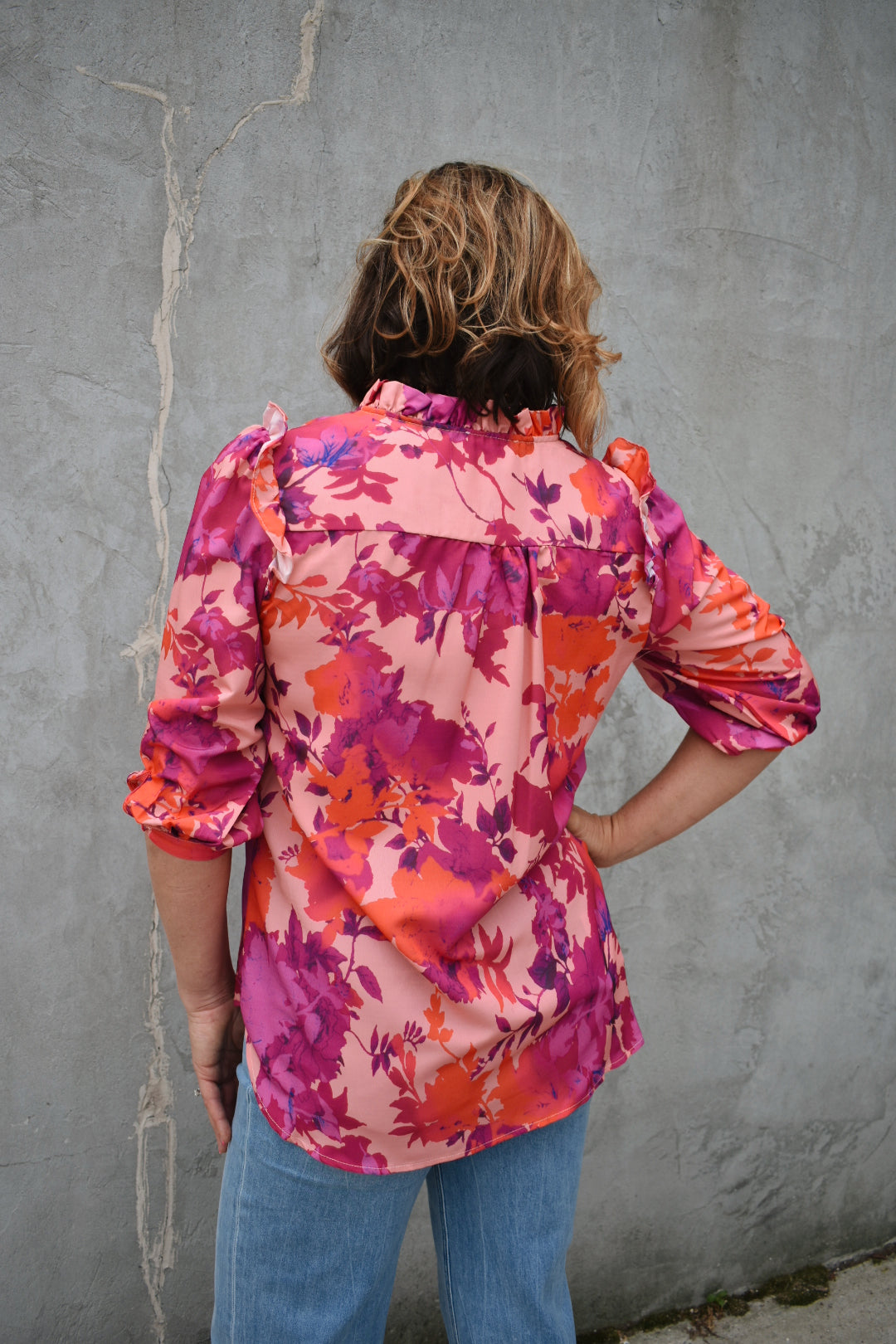 fuchsia, orange, light purple, and blush patterned button down blouse. ruffled V-neckline and ruffled shoulder detailing. Button-cuffed 3/4 sleeves. The brand is First Love.