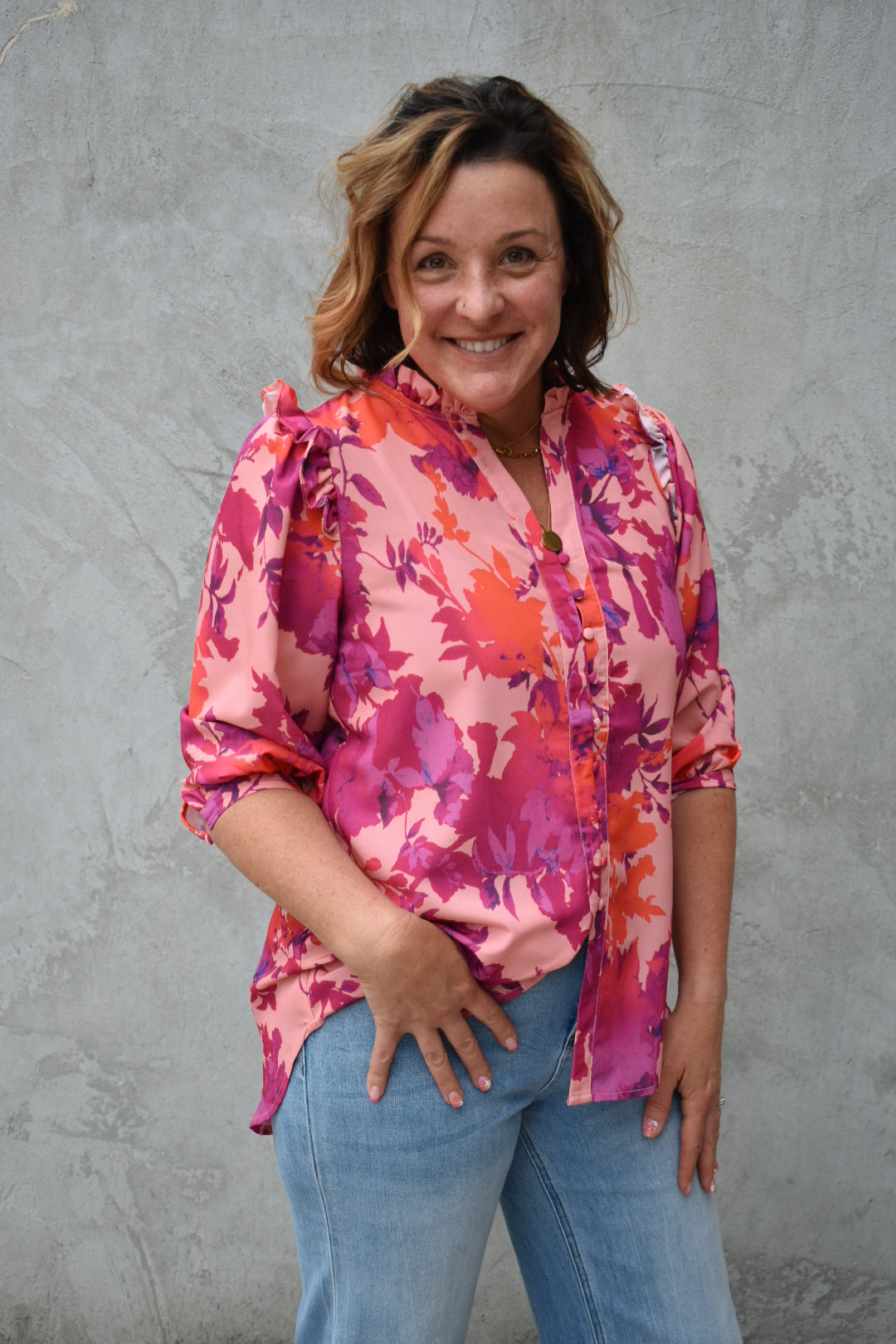 fuchsia, orange, light purple, and blush patterned button down blouse. ruffled V-neckline and ruffled shoulder detailing. Button-cuffed 3/4 sleeves. The brand is First Love.