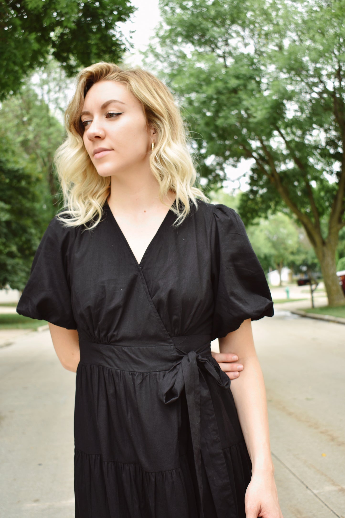 Black wrap dress with short puff sleeves and tiered midi skirt. Snap enclosure on bust and button enclosure on waist.