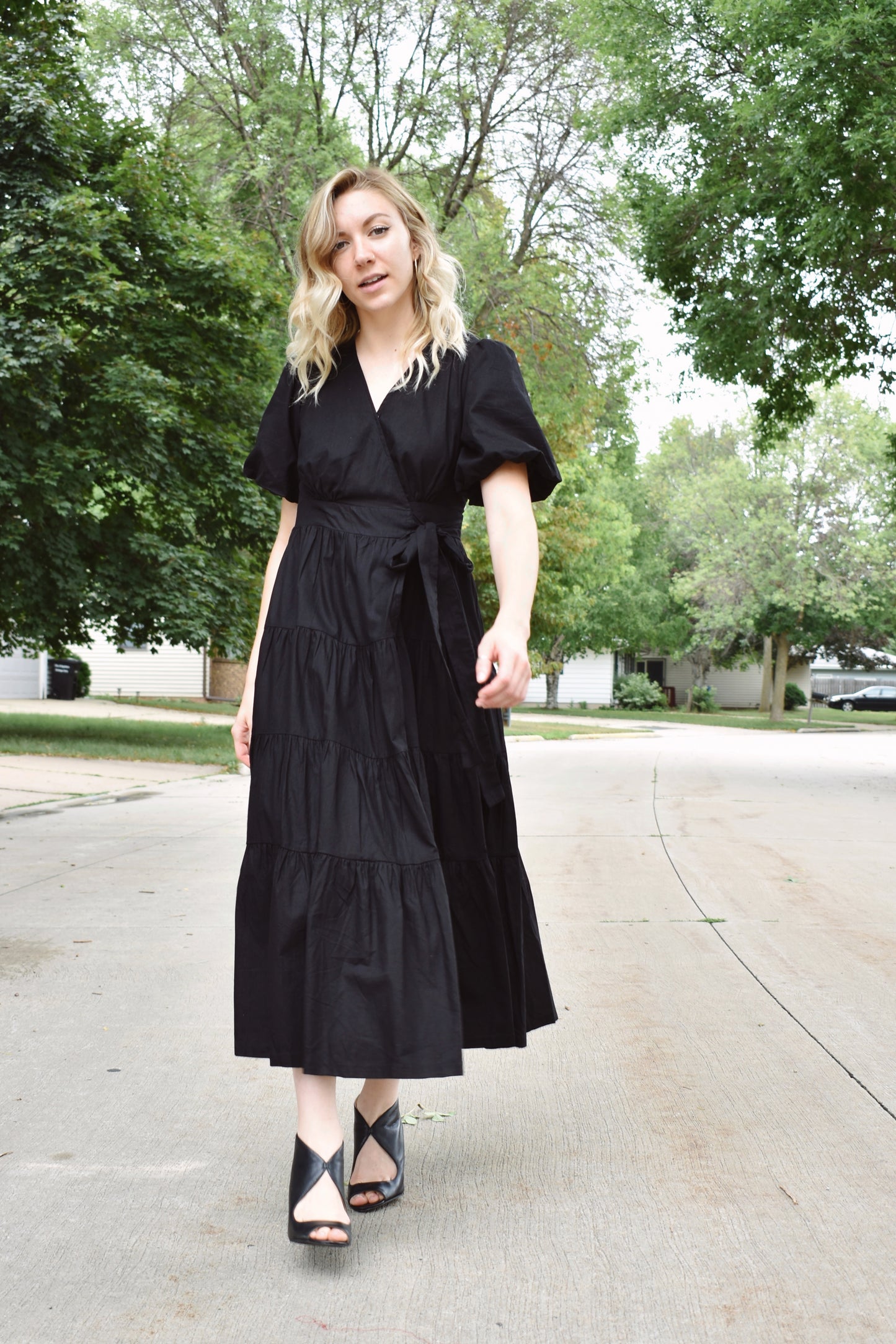 Black wrap dress with short puff sleeves and tiered midi skirt. Snap enclosure on bust and button enclosure on waist.