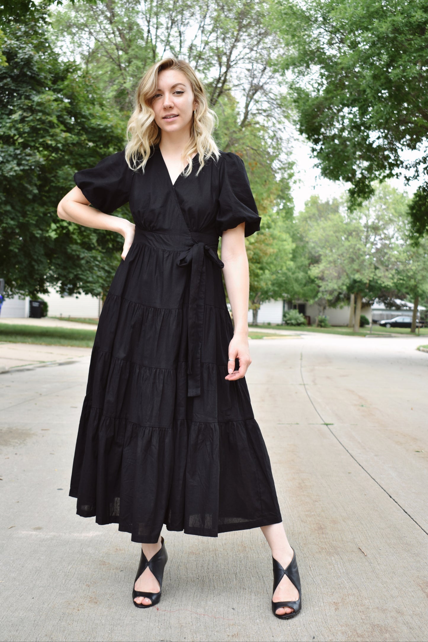 Black wrap dress with short puff sleeves and tiered midi skirt. Snap enclosure on bust and button enclosure on waist.