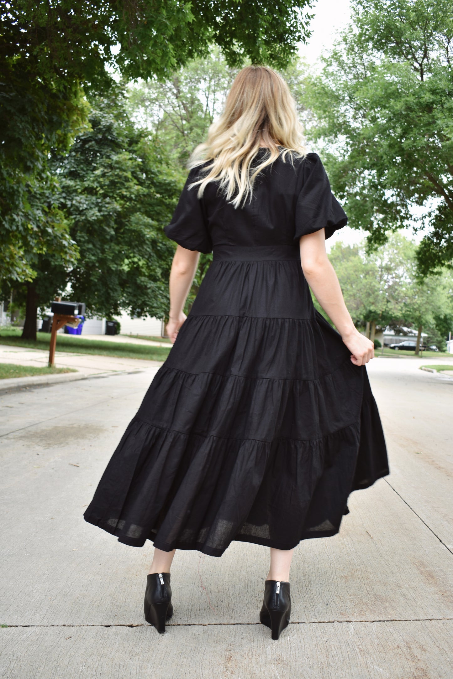 Black wrap dress with short puff sleeves and tiered midi skirt. Snap enclosure on bust and button enclosure on waist.