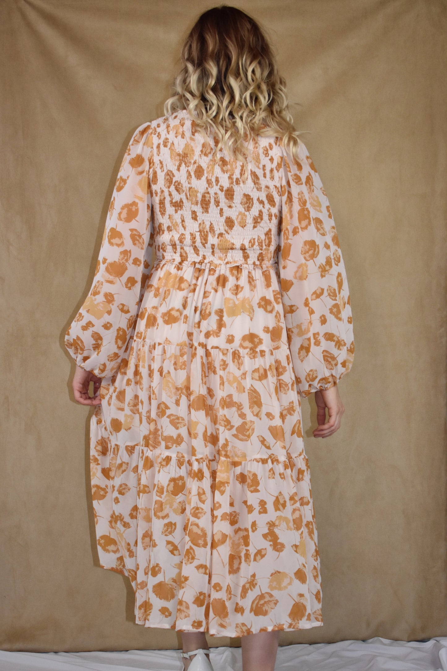 long sleeve midi dress with v neck. printed chiffon fabric infused with flower petals. tiered skirt and smocking detail on bodice. cream and mustard colors.