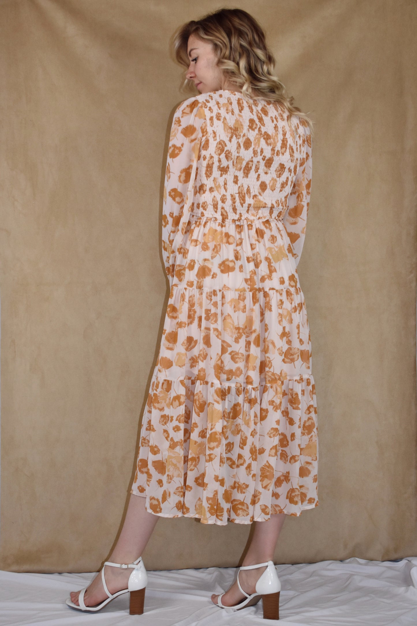 long sleeve midi dress with v neck. printed chiffon fabric infused with flower petals. tiered skirt and smocking detail on bodice. cream and mustard colors.