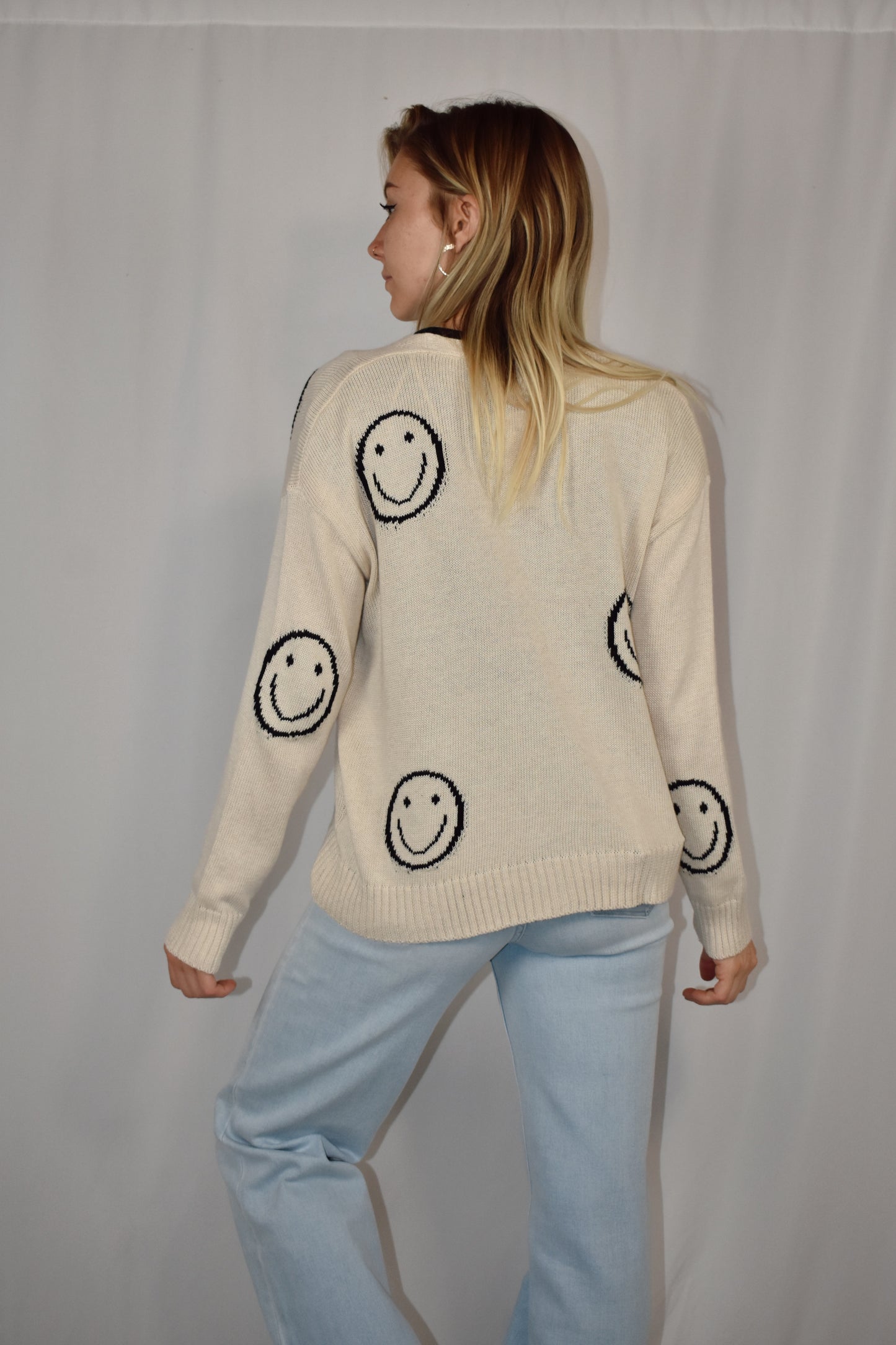 Button down cardigan in a neutral color with big black smiley faces and two patch pockets on the front. Waist length
