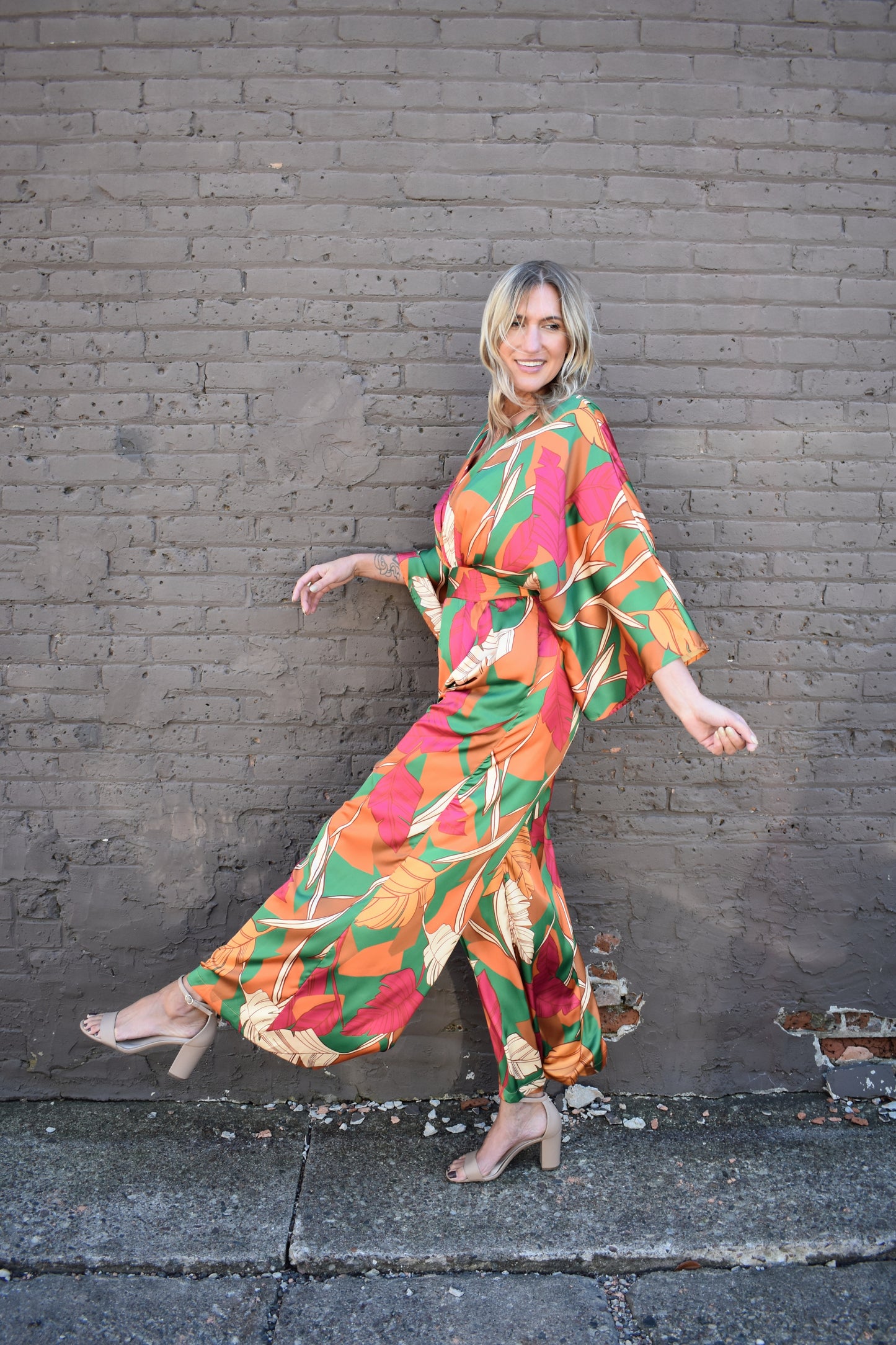 statement satin jumpsuit with a green, rust, cream and pink color scheme. V neckline, kimono sleeves, wide waistband, side pockets, center back slit with button closure on back of neck. wide leg.