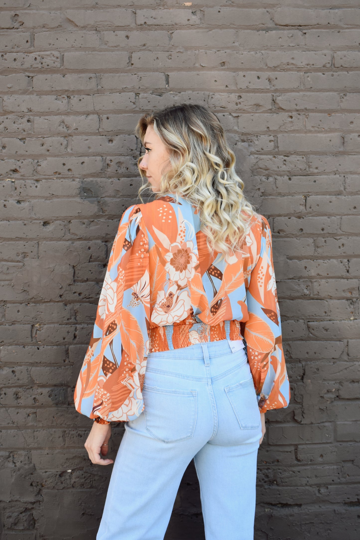 light blue and shades of orange printed lightweight long sleeve v neck line top with twist detail in front and smocked cuffs with balloon sleeves. smocked back waistband.