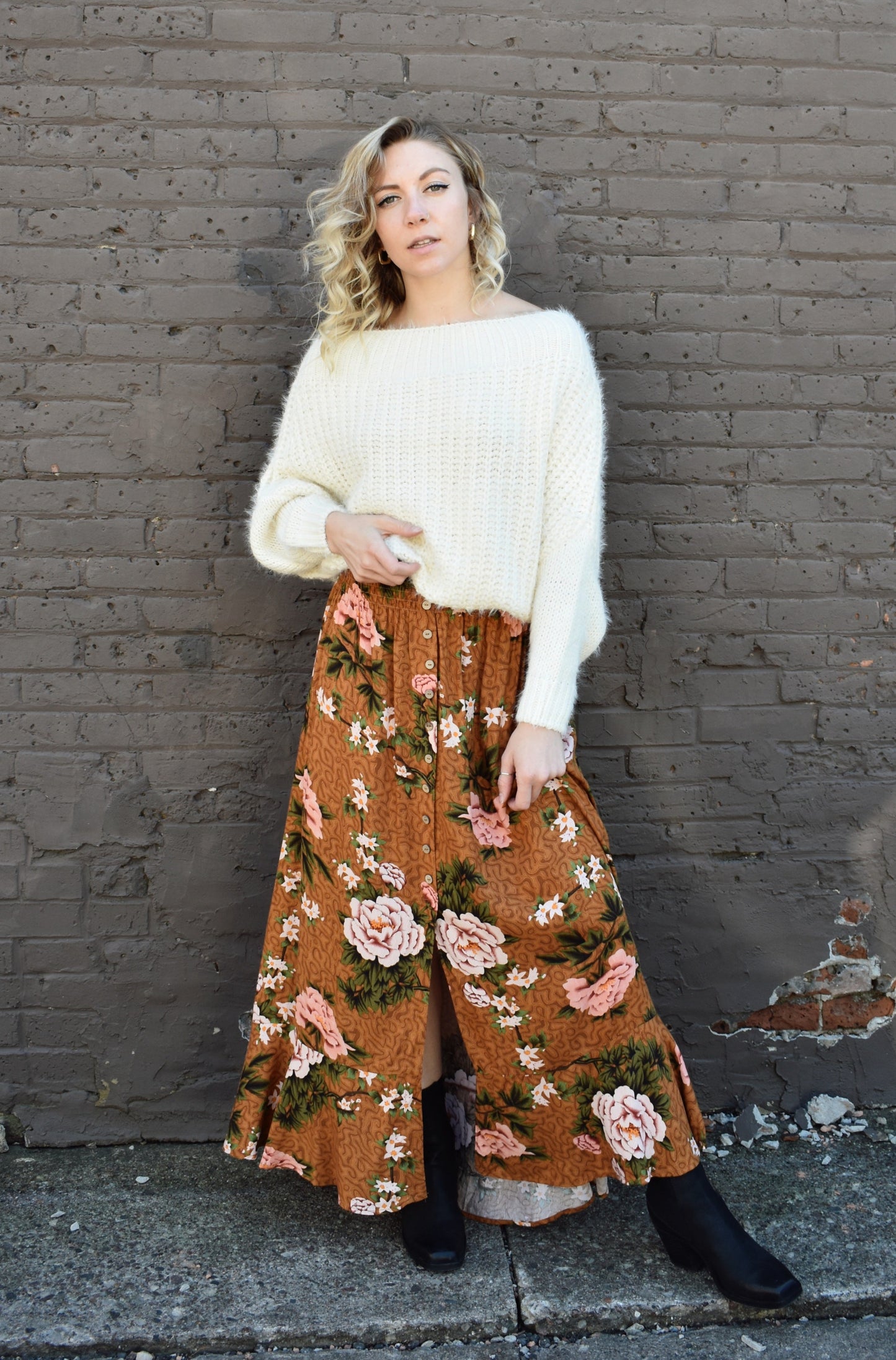 Floral printed maxi skirt with a 3/4 button down front that leads into a center slit. slight ruffle at the bottom. elastic waistband. light brown/rust color background with big printed white and blush colored flowers with green stems.