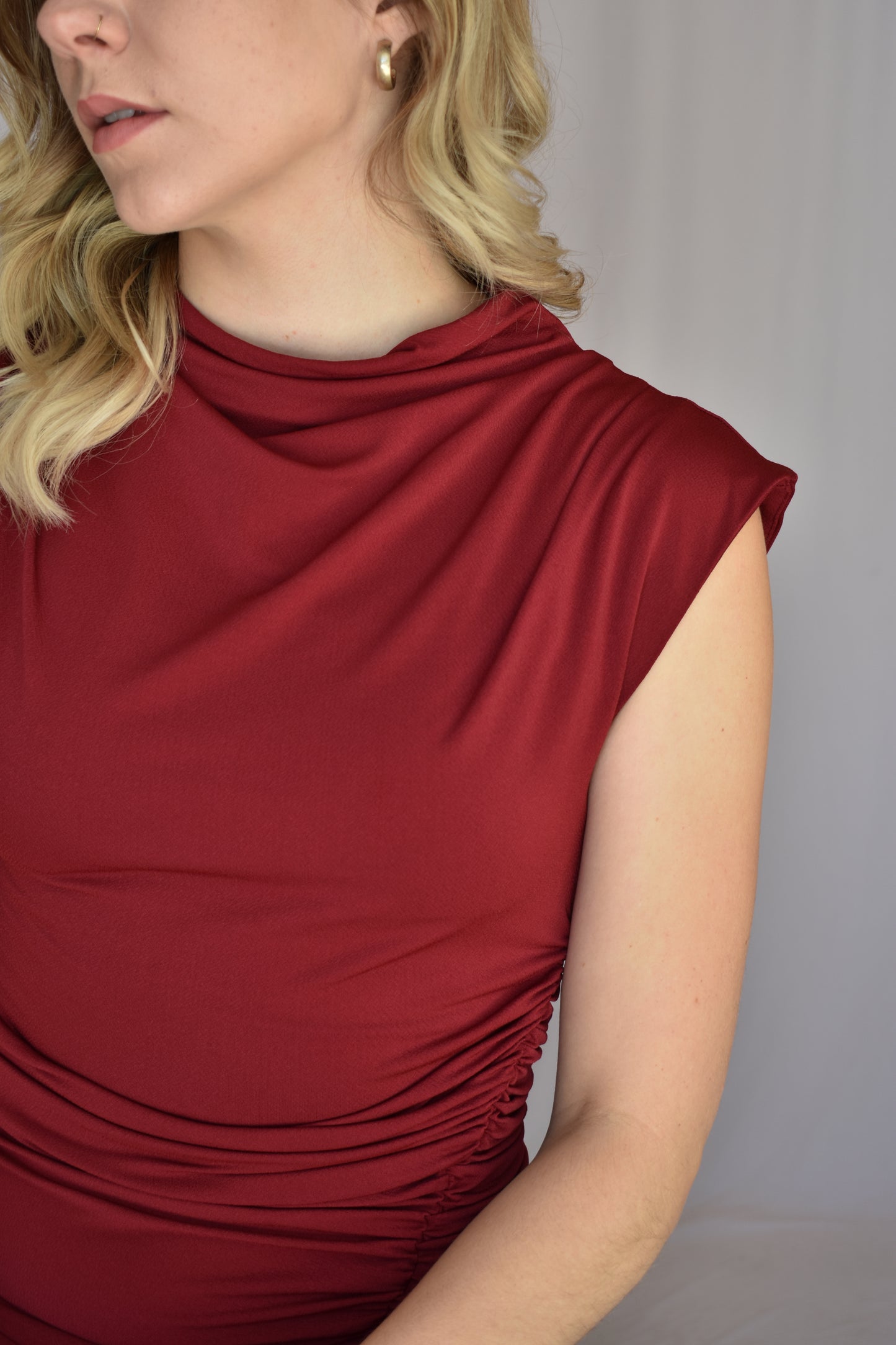 burgundy midi dress. form fitting with slit up left side with rushing detail on the side of the bodice. cap sleeves with mock neck and draping detail in fabric across chest. Stretch fabric.