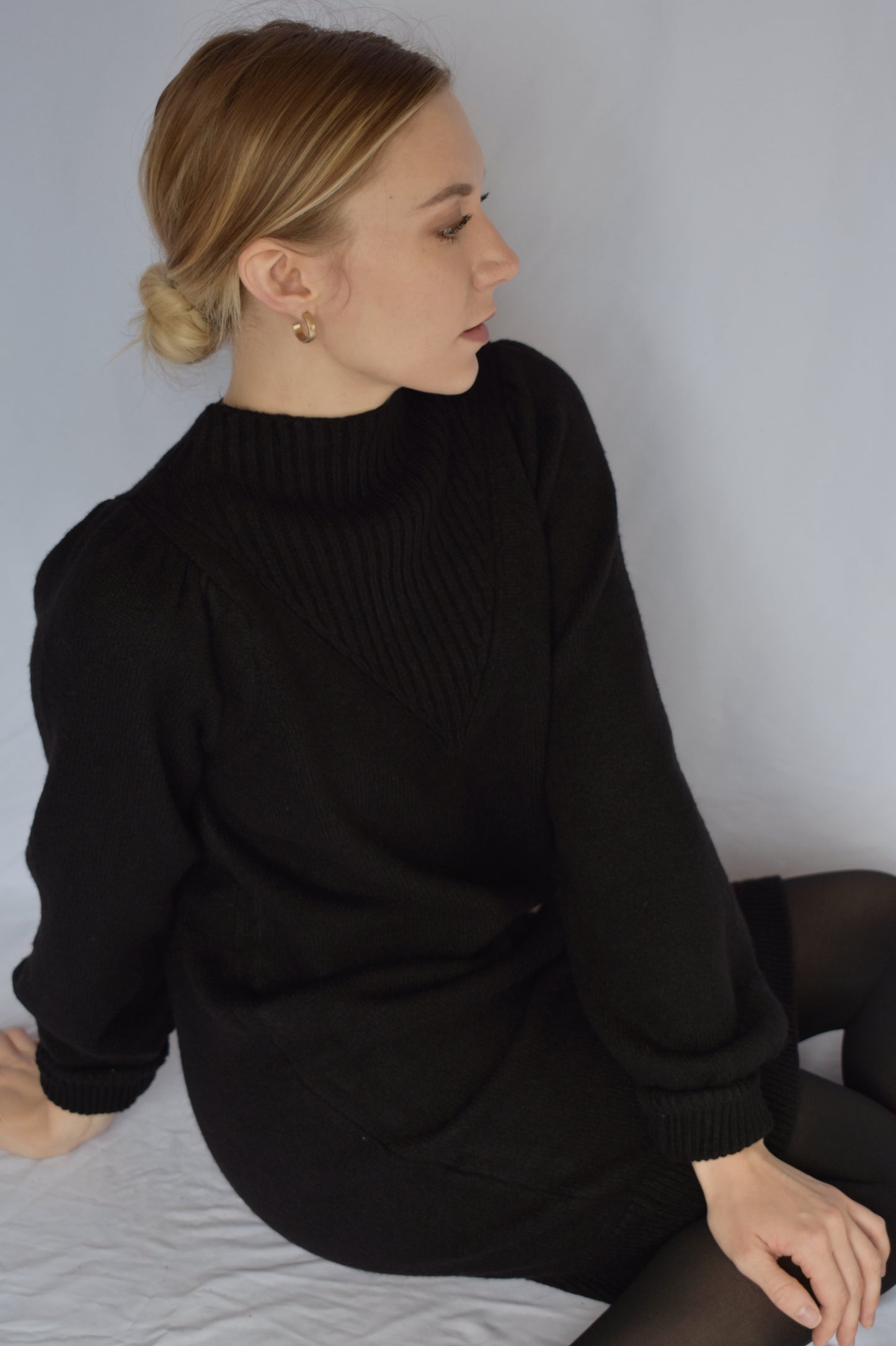 black sweater dress with long sleeves. ribbed cuffs and mock neck with v neck ribbed detail. slight puff on shoulders. hits just above the knees. relaxed fit, not oversized.