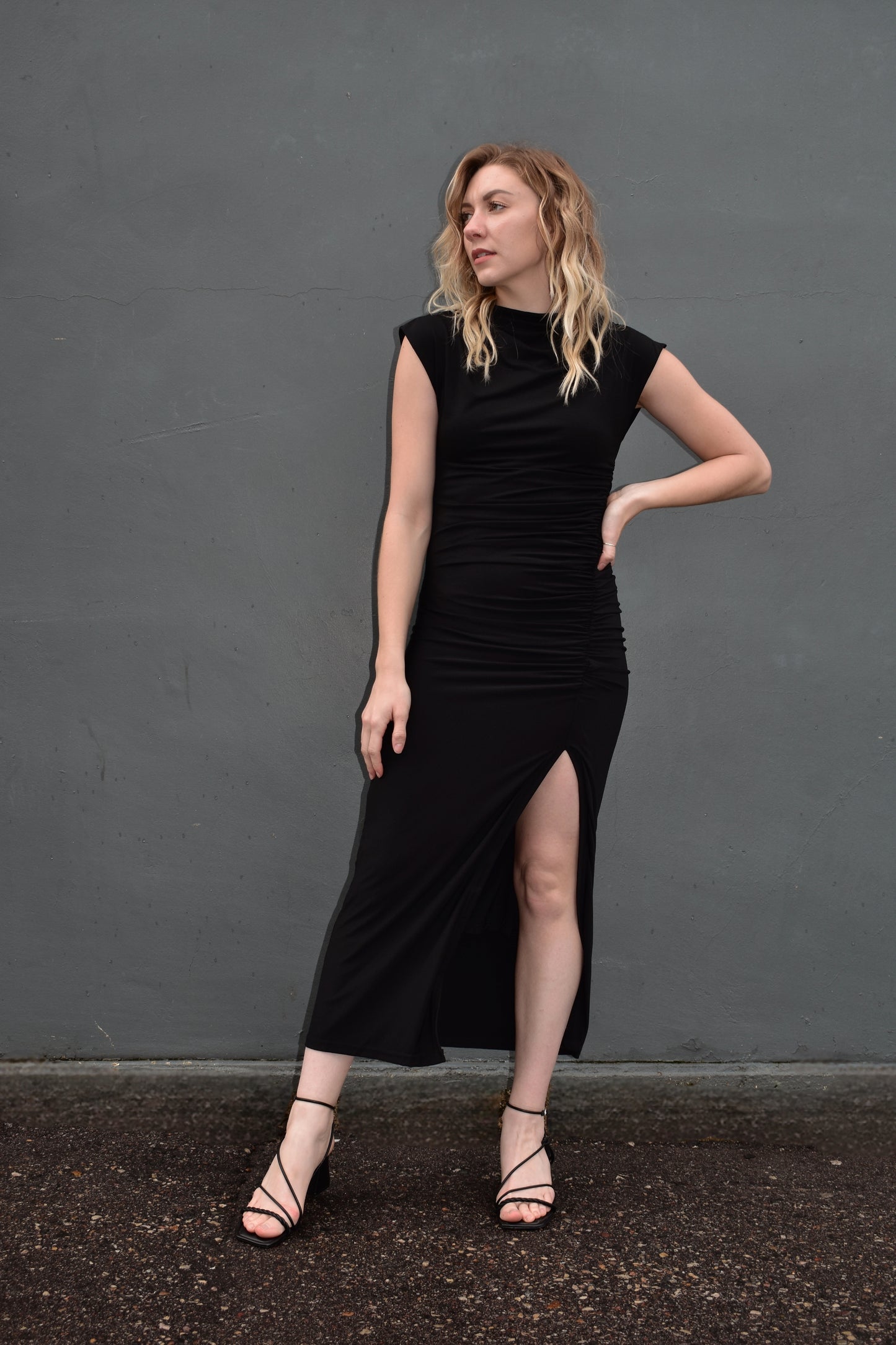black midi dress. form fitting with slit up left side with rushing detail on the side of the bodice. cap sleeves with mock neck and draping detail in fabric across chest. Stretch fabric.