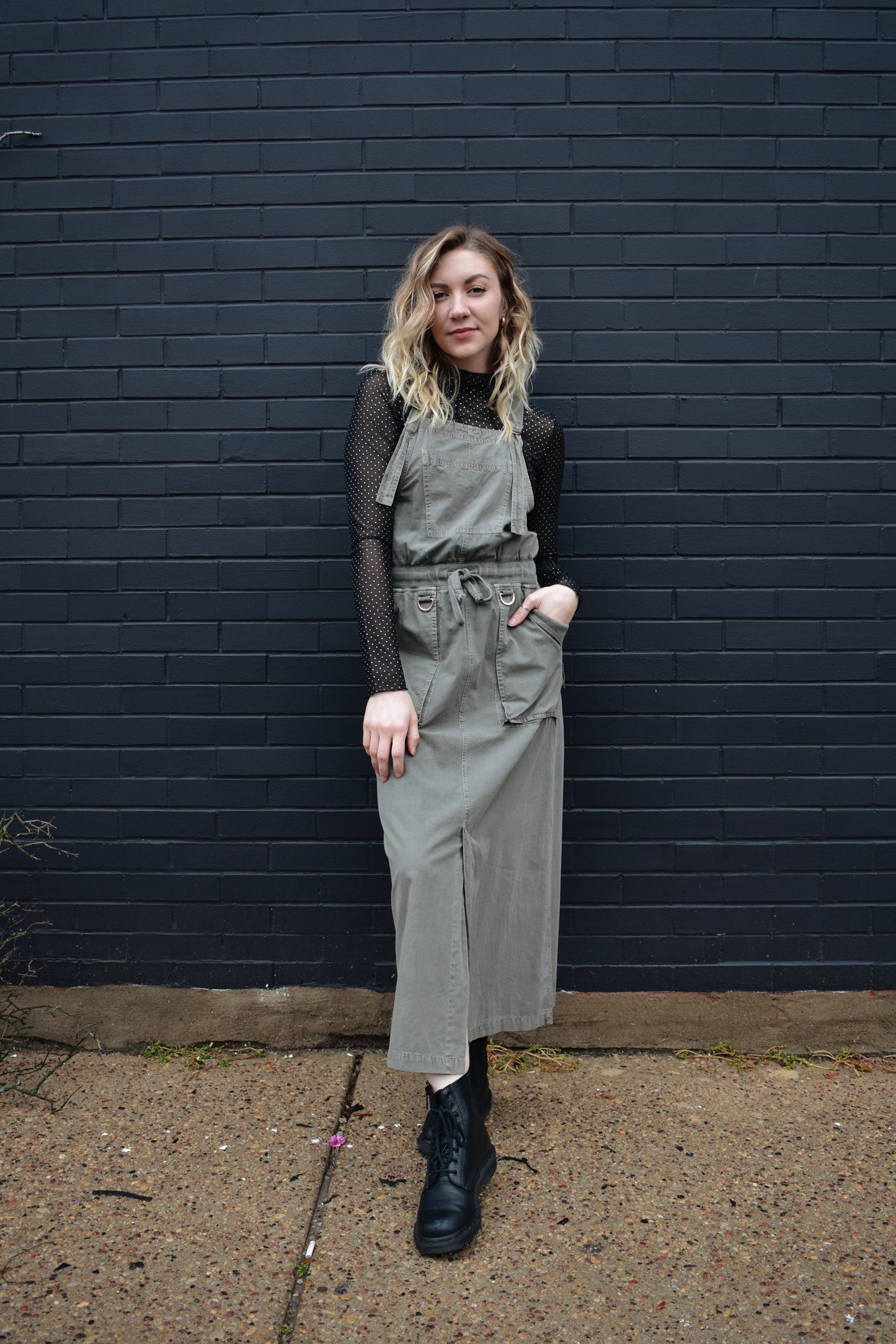 olive overall dress, midi length, adjustable straps, waist drawstring, front slit up skirt, front and back patch pockets, and a pocket on the front.