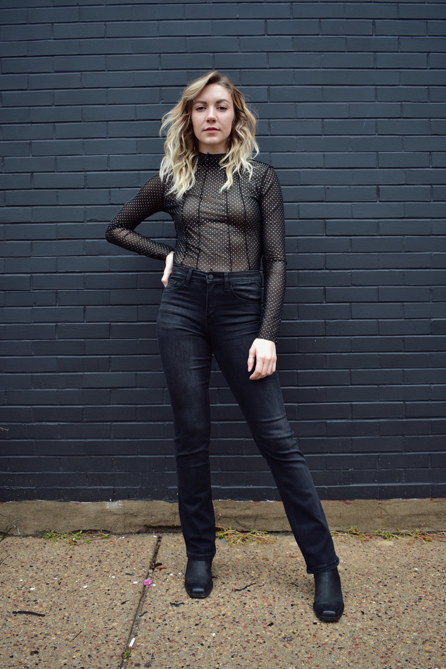 Black mesh mock neck long sleeve top with exposed seams down the front and back and a textured silver dot pattern, full length.