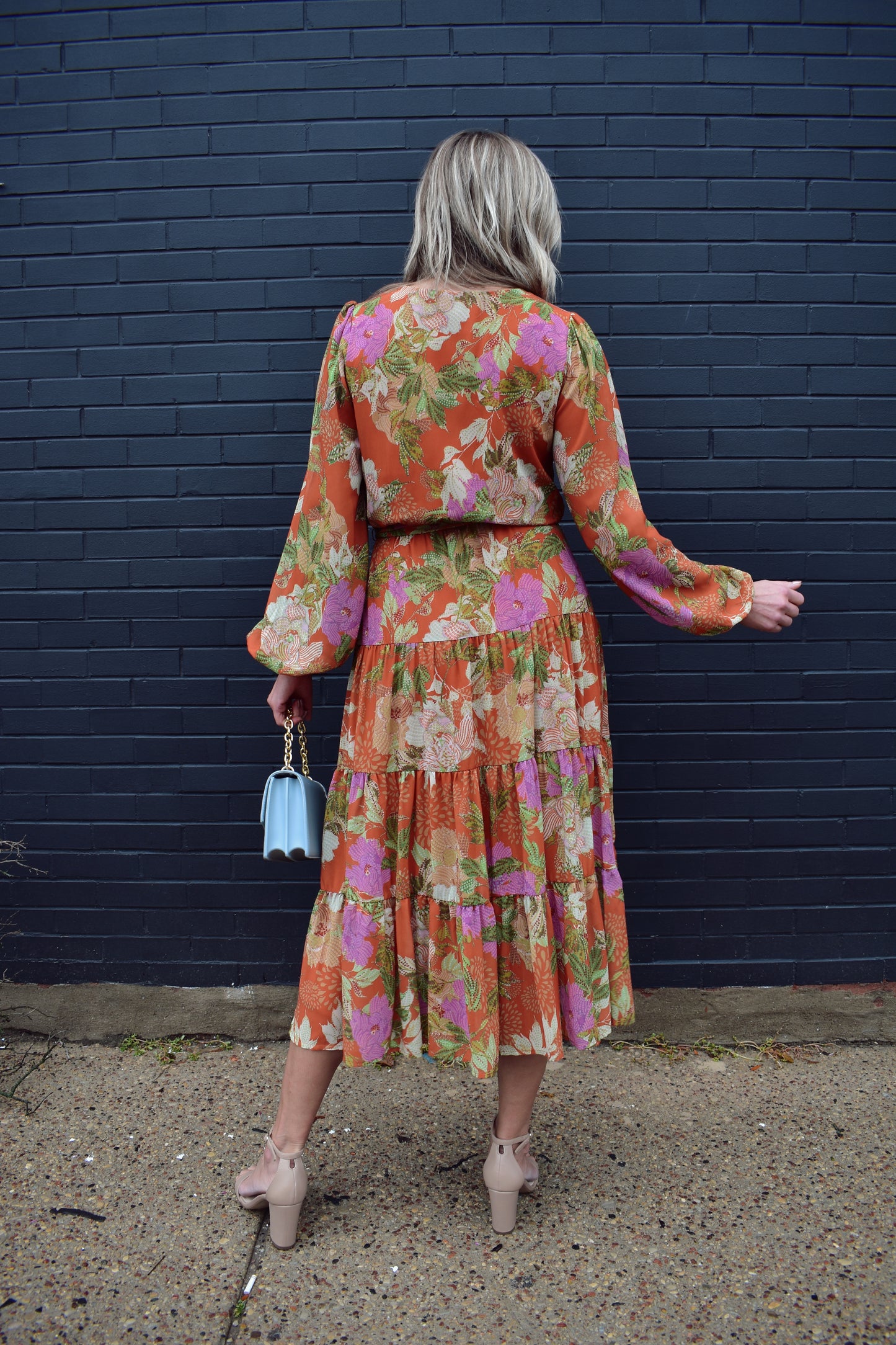 Long sleeve midi dress with floral print. Colors are an orange background with yellow, purple, light pink, green, white and cream. Wrap V neckline, lightweight fabric with lining, elastic at wrists, wrap at waist, tiered skirt.