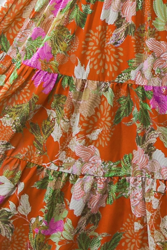 Long sleeve midi dress with floral print. Colors are an orange background with yellow, purple, light pink, green, white and cream. Wrap V neckline, lightweight fabric with lining, elastic at wrists, wrap at waist, tiered skirt.