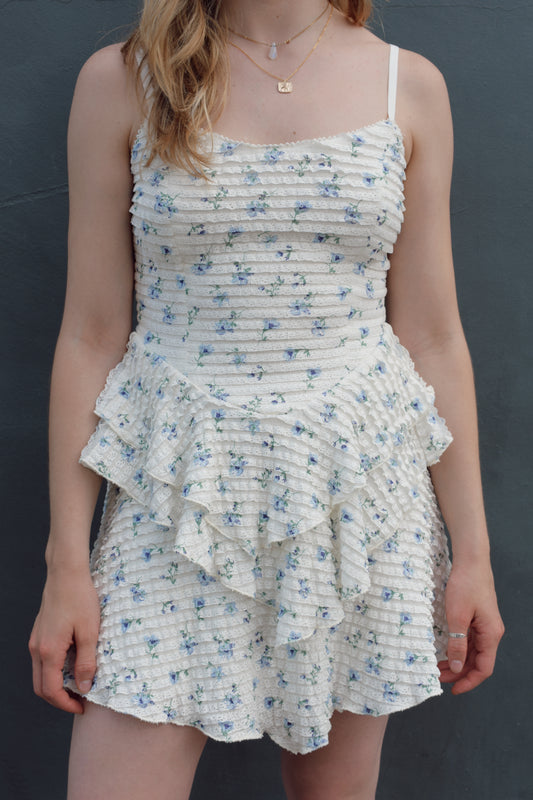 cream mini dress with a blue ditsy floral pattern and mini ruffle fabric, stretchy, back zip enclosure, adjustable spaghetti straps, shark bite tiered skirt, fitted bodice, lined