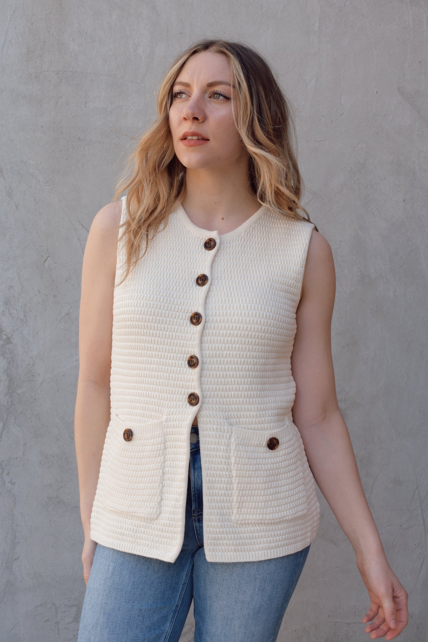 cream full length knit summer sweater vest with front slit and brown button enclosure crew neck when fully buttoned patch pockets with front button detail