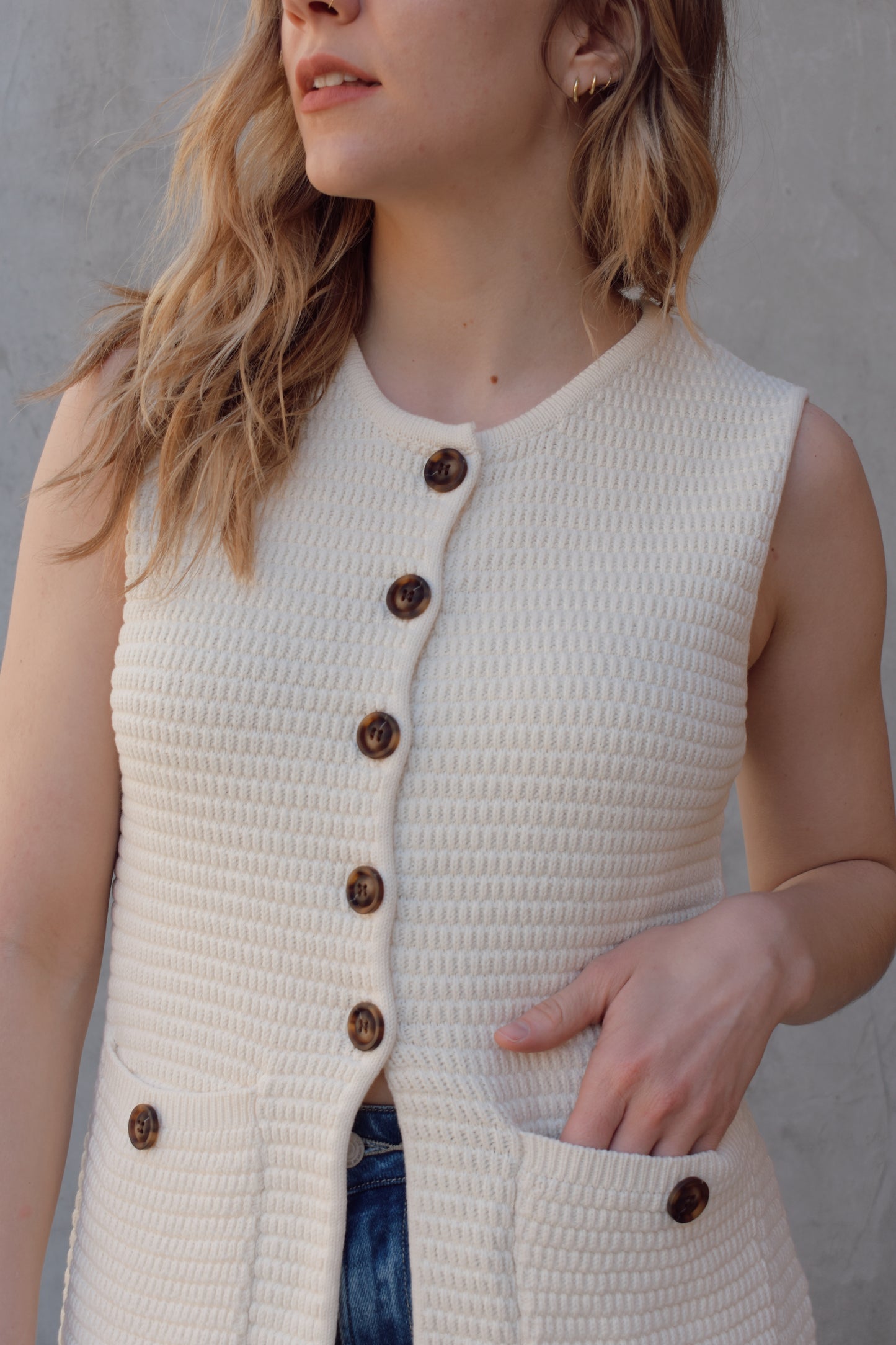 cream full length knit summer sweater vest with front slit and brown button enclosure crew neck when fully buttoned patch pockets with front button detail