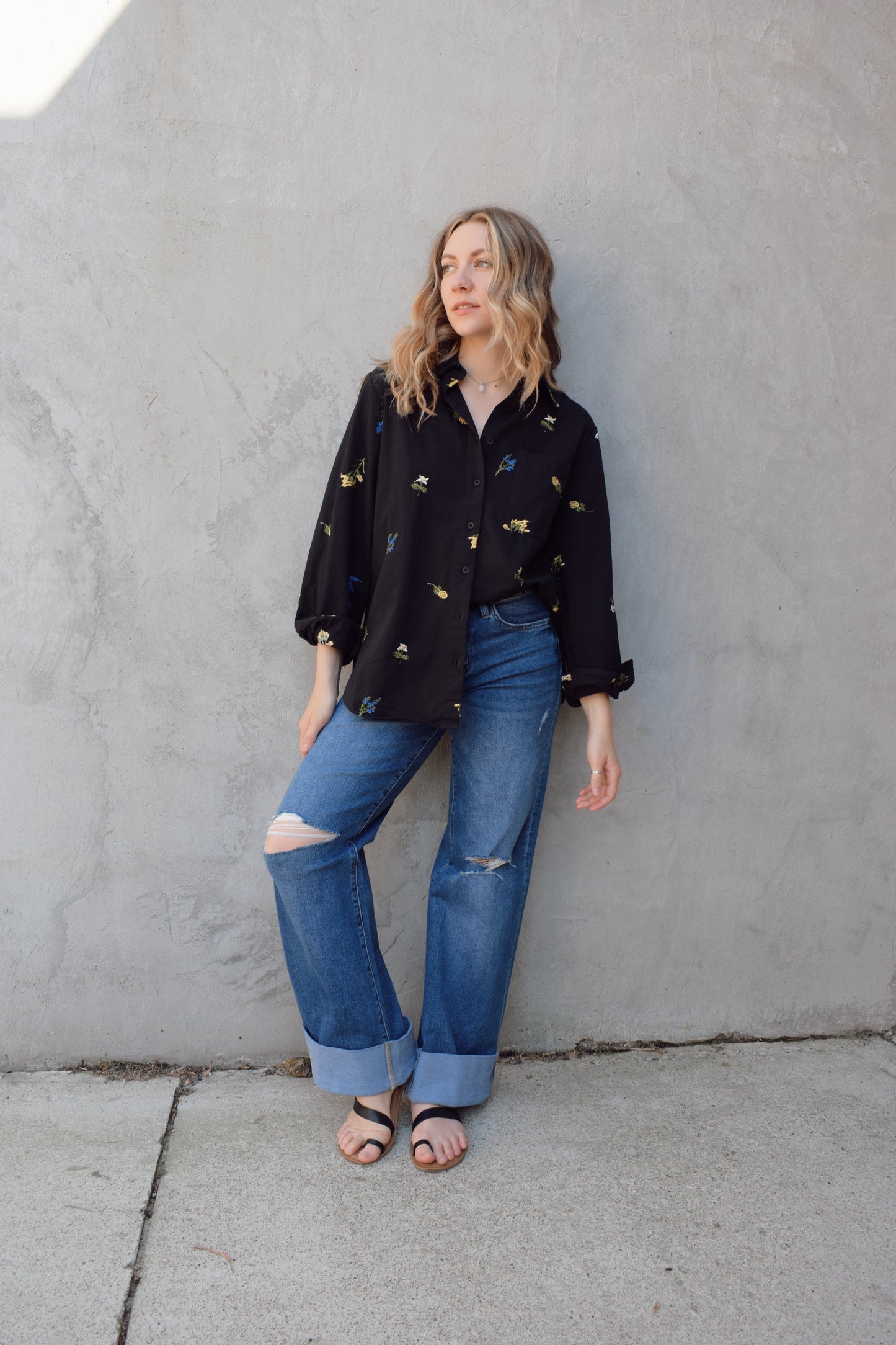 oversized black button down with flowers embroidered on front, back, and sleeves. Flowers are green, blue, yellow, white. Shirt tail hem, buttoned cuffs, one patch breast pockets, collared neckline, black buttons.