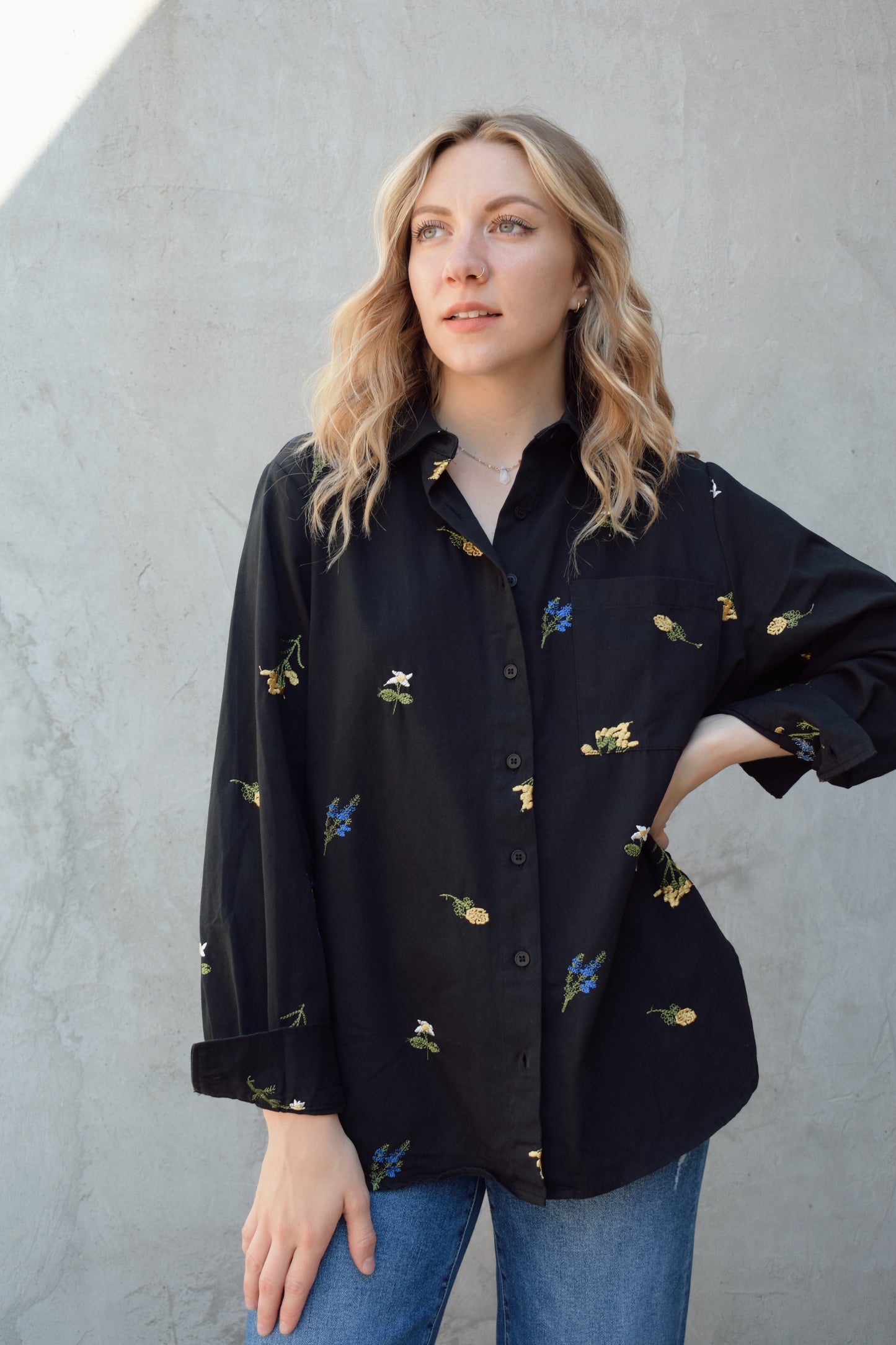 oversized black button down with flowers embroidered on front, back, and sleeves. Flowers are green, blue, yellow, white. Shirt tail hem, buttoned cuffs, one patch breast pockets, collared neckline, black buttons.
