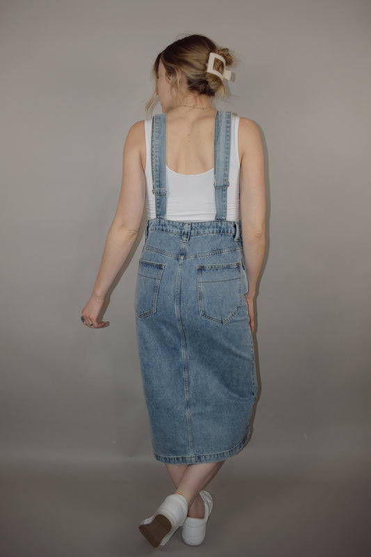 light wash denim overall midi skirt dress with front slit, square neckline on front and back, adjustable straps, has beltloops, deep front pockets, back pockets, button enclosure on both sides