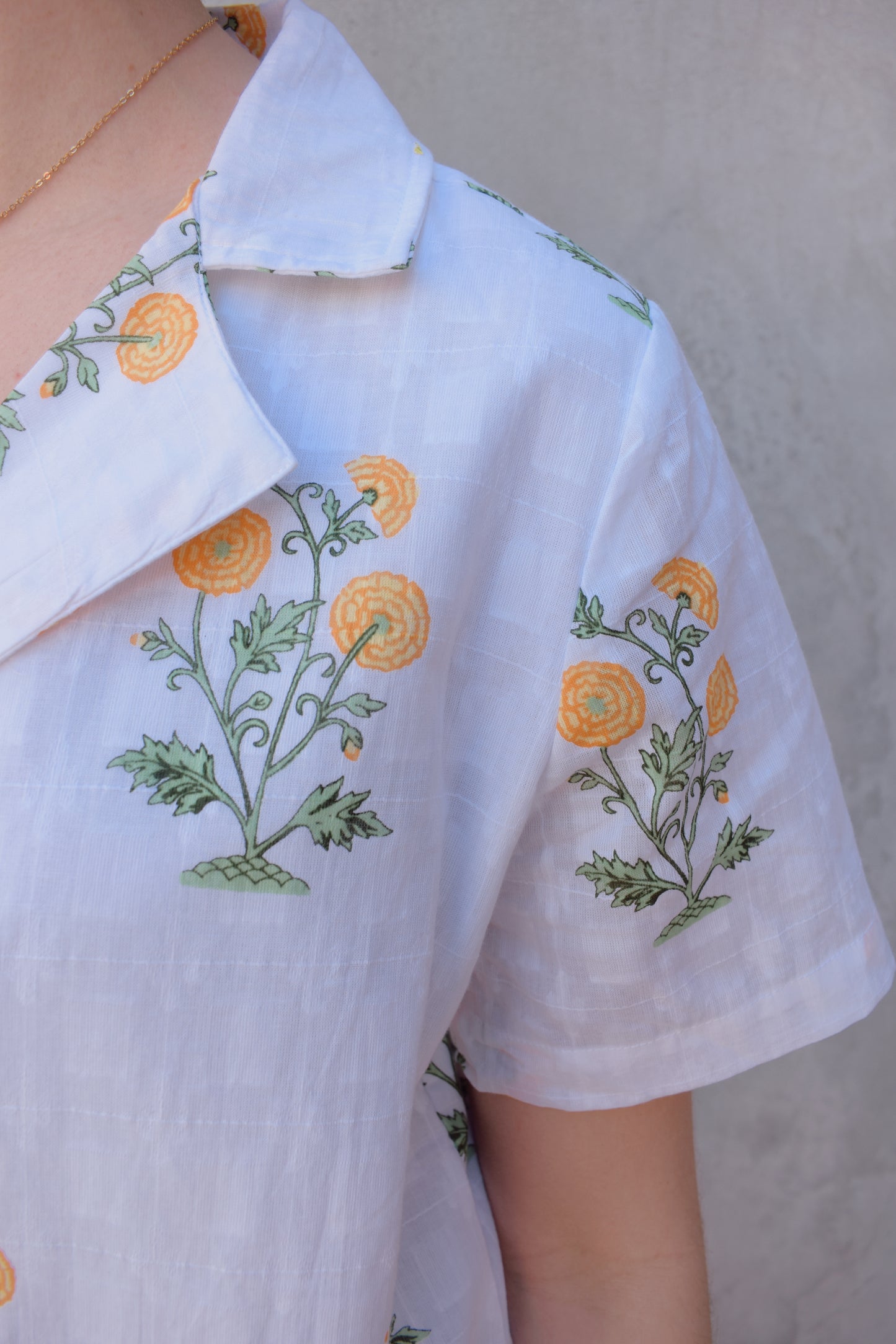 white v neck short sleeve button down with a marigold embroidered pattern. full length, straight fit. 100% cotton