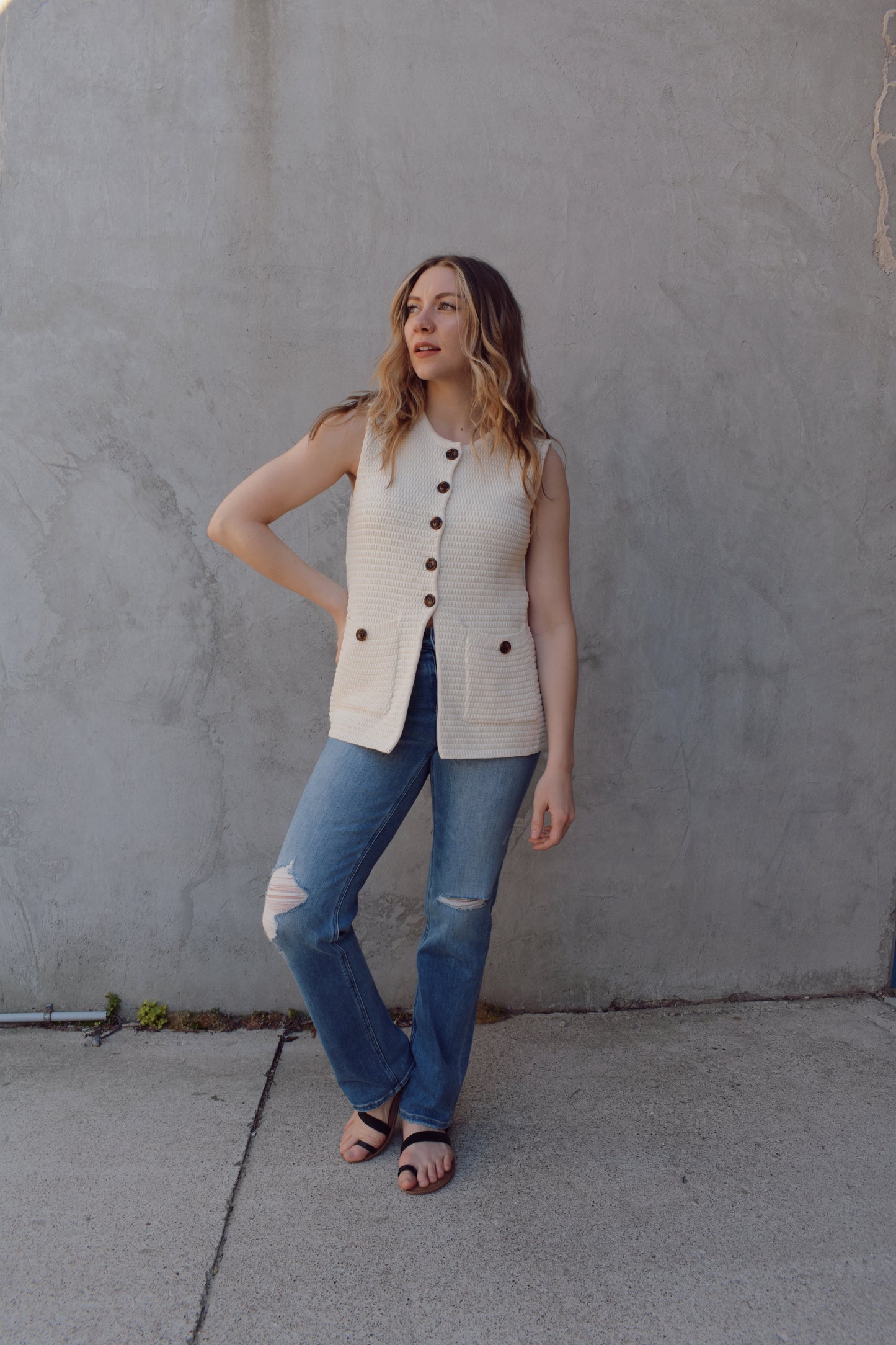 cream full length knit summer sweater vest with front slit and brown button enclosure crew neck when fully buttoned patch pockets with front button detail