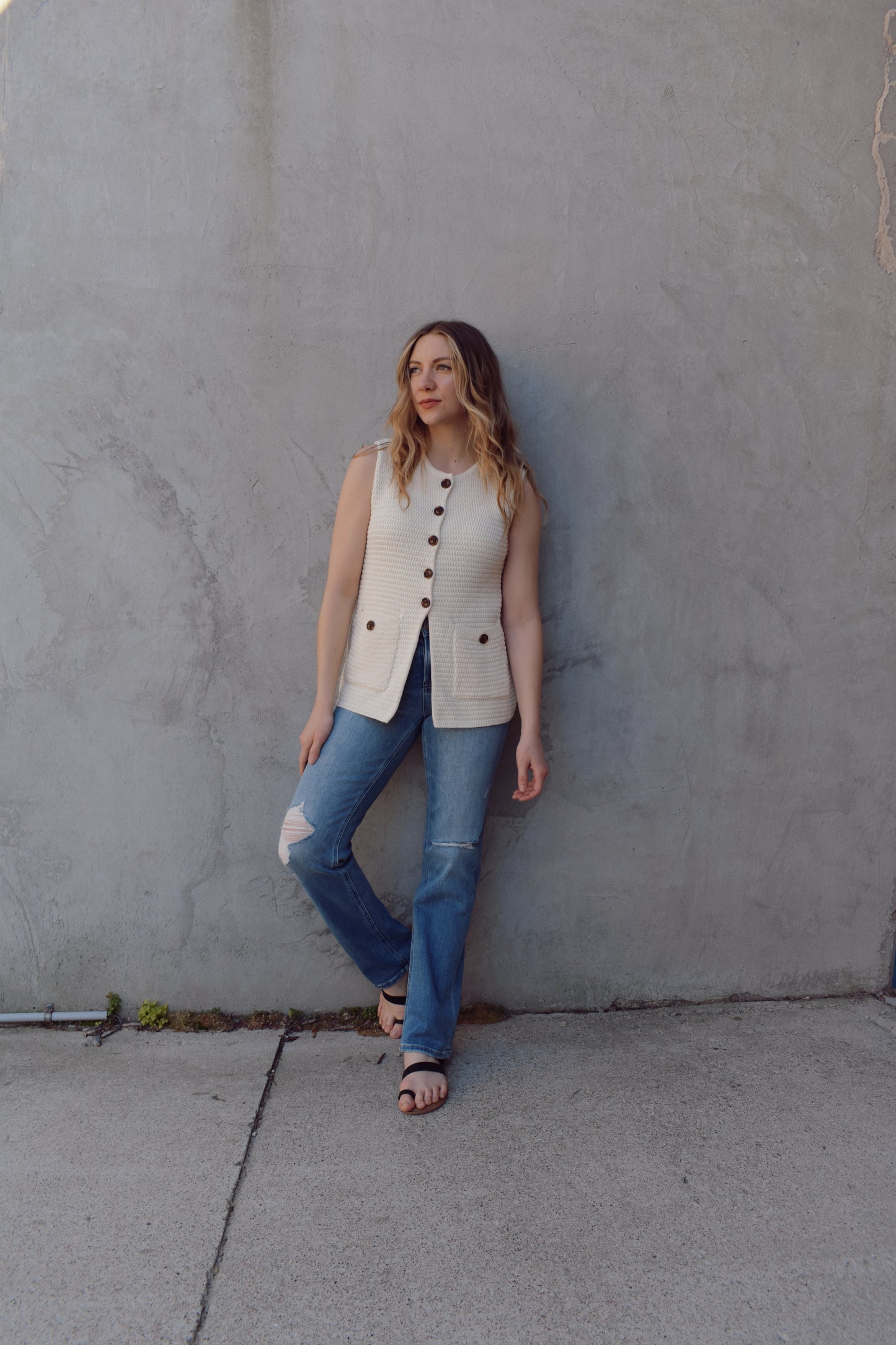 cream full length knit summer sweater vest with front slit and brown button enclosure crew neck when fully buttoned patch pockets with front button detail