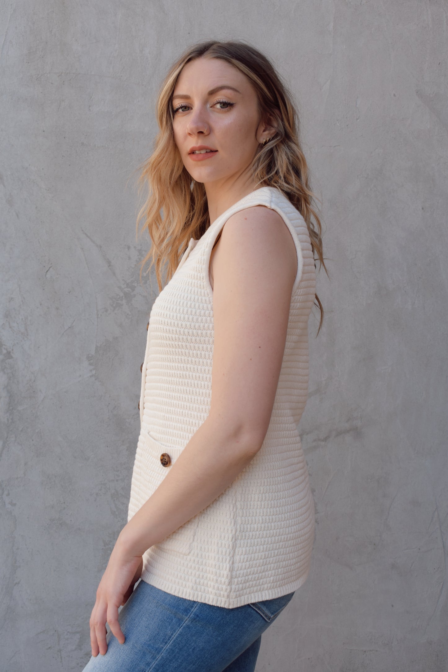cream full length knit summer sweater vest with front slit and brown button enclosure crew neck when fully buttoned patch pockets with front button detail