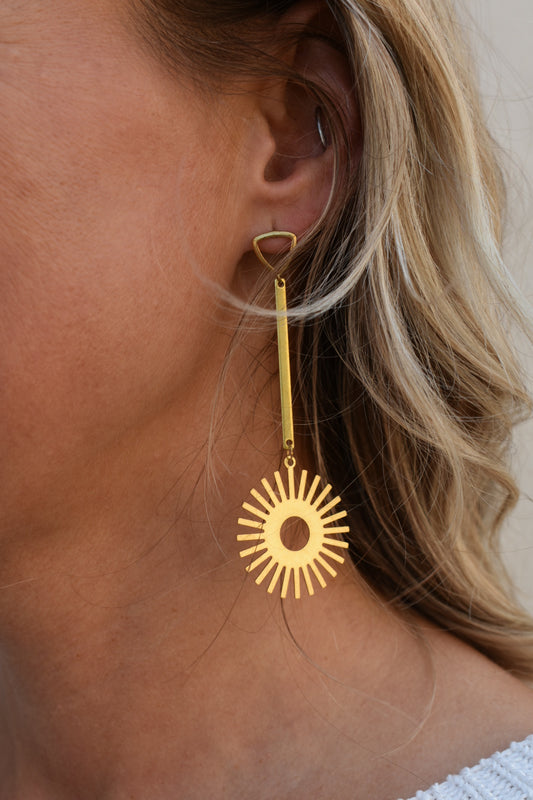 laser cut brass geometric sun pendants set against a brass bar and suspended from bright brass triangle shaped studs gold earrings the revival