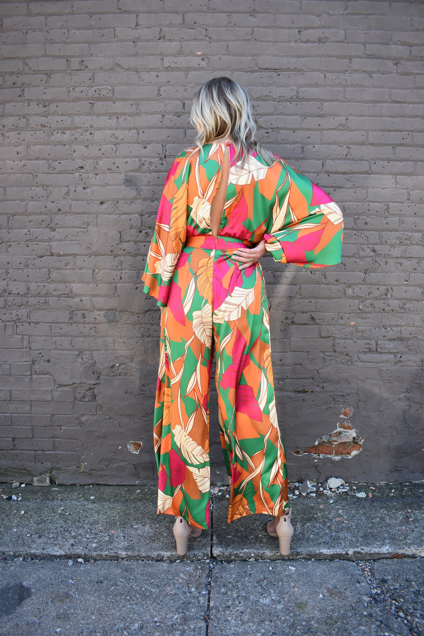 statement satin jumpsuit with a green, rust, cream and pink color scheme. V neckline, kimono sleeves, wide waistband, side pockets, center back slit with button closure on back of neck. wide leg. 