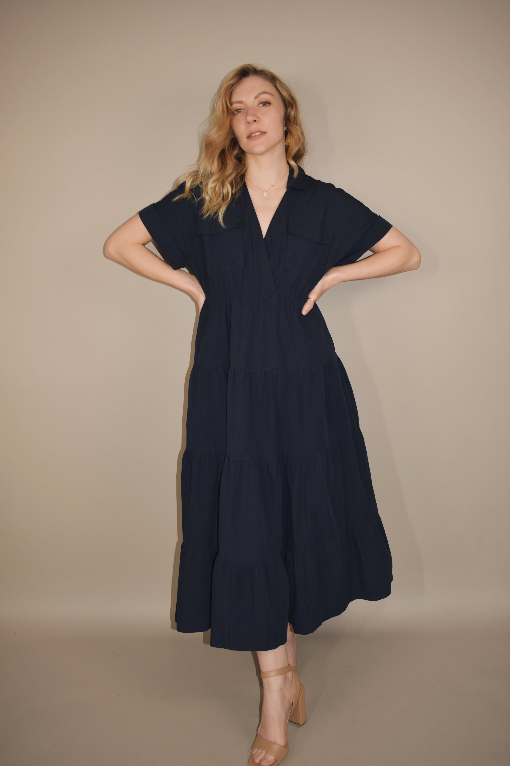 navy blue midi dress with tiered skirt and synched waist. drop shoulder cuffed short sleeves with v neck. collar and two flap enclosure faux breast pockets. has side pockets in skirt of dress.