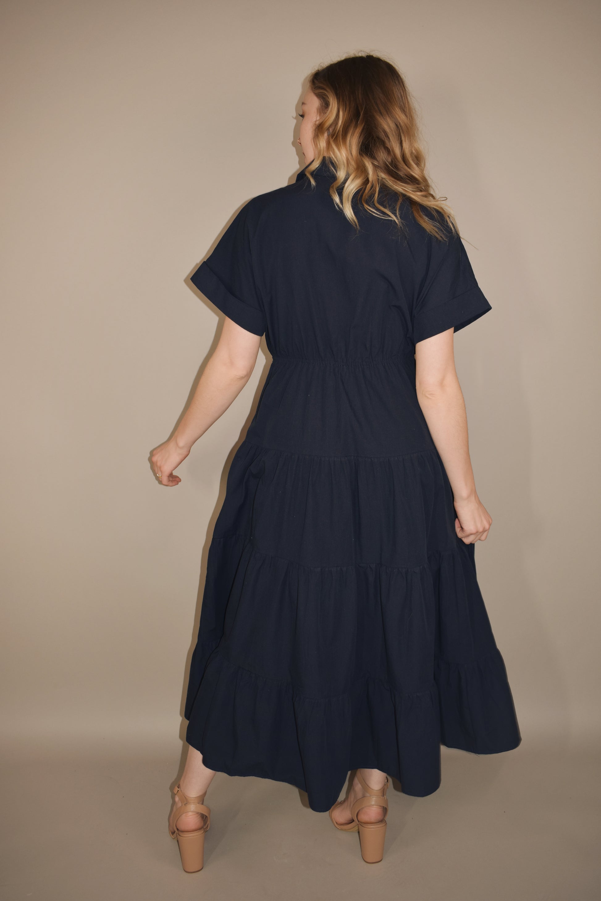 navy blue midi dress with tiered skirt and synched waist. drop shoulder cuffed short sleeves with v neck. collar and two flap enclosure faux breast pockets. has side pockets in skirt of dress.