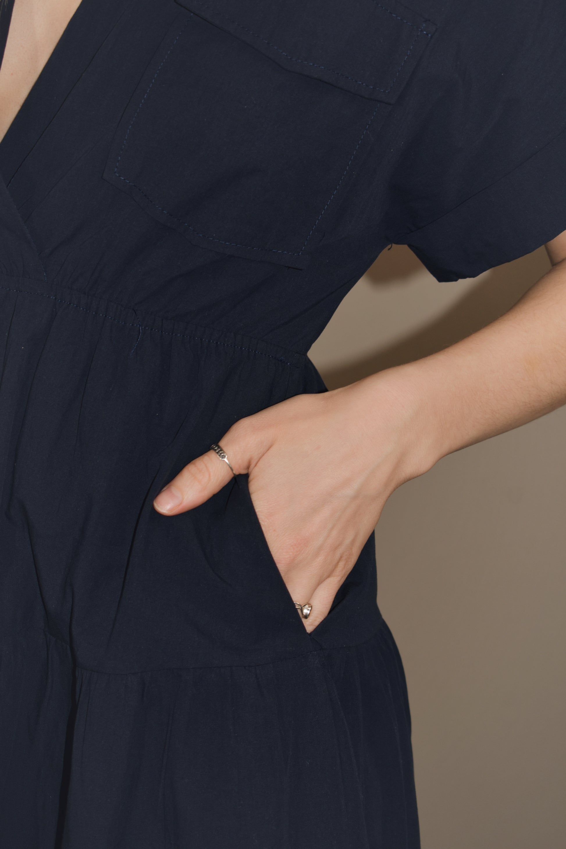 navy blue midi dress with tiered skirt and synched waist. drop shoulder cuffed short sleeves with v neck. collar and two flap enclosure faux breast pockets. has side pockets in skirt of dress.