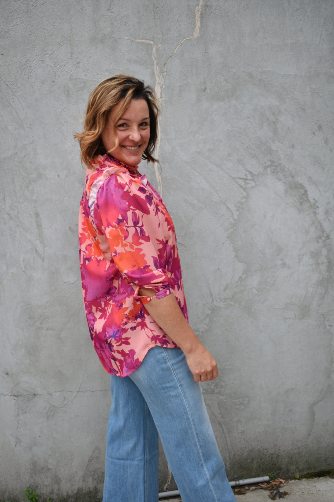 fuchsia, orange, light purple, and blush patterned button down blouse. ruffled V-neckline and ruffled shoulder detailing. Button-cuffed 3/4 sleeves. The brand is First Love.
