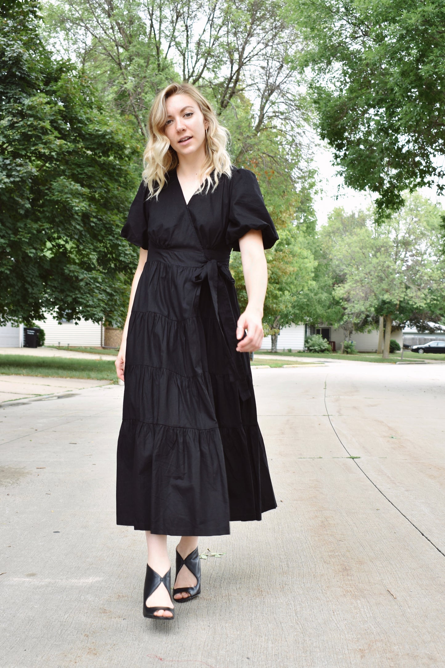 Black wrap dress with short puff sleeves and tiered midi skirt. Snap enclosure on bust and button enclosure on waist. 