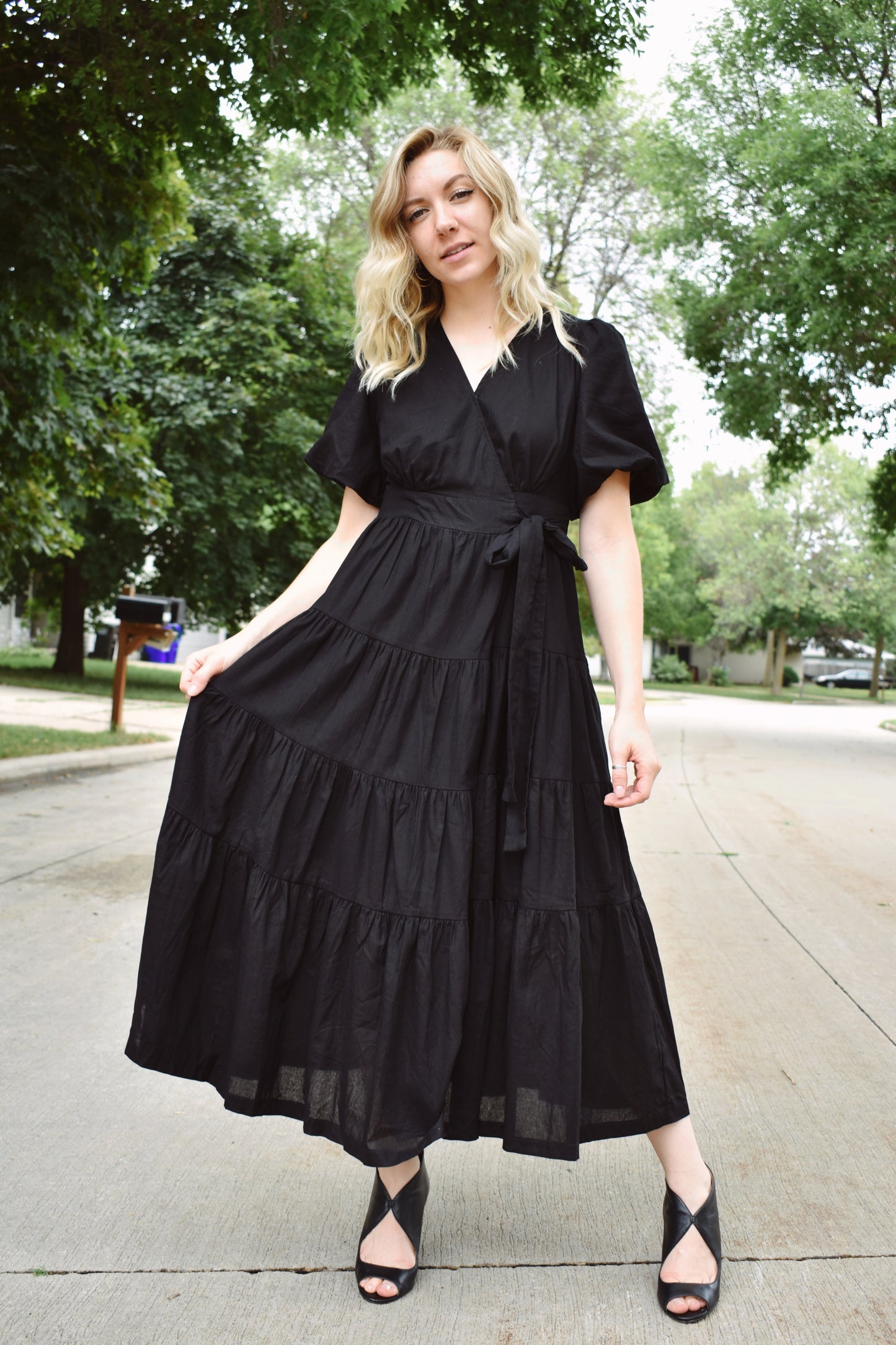 Black wrap dress with short puff sleeves and tiered midi skirt. Snap enclosure on bust and button enclosure on waist. 