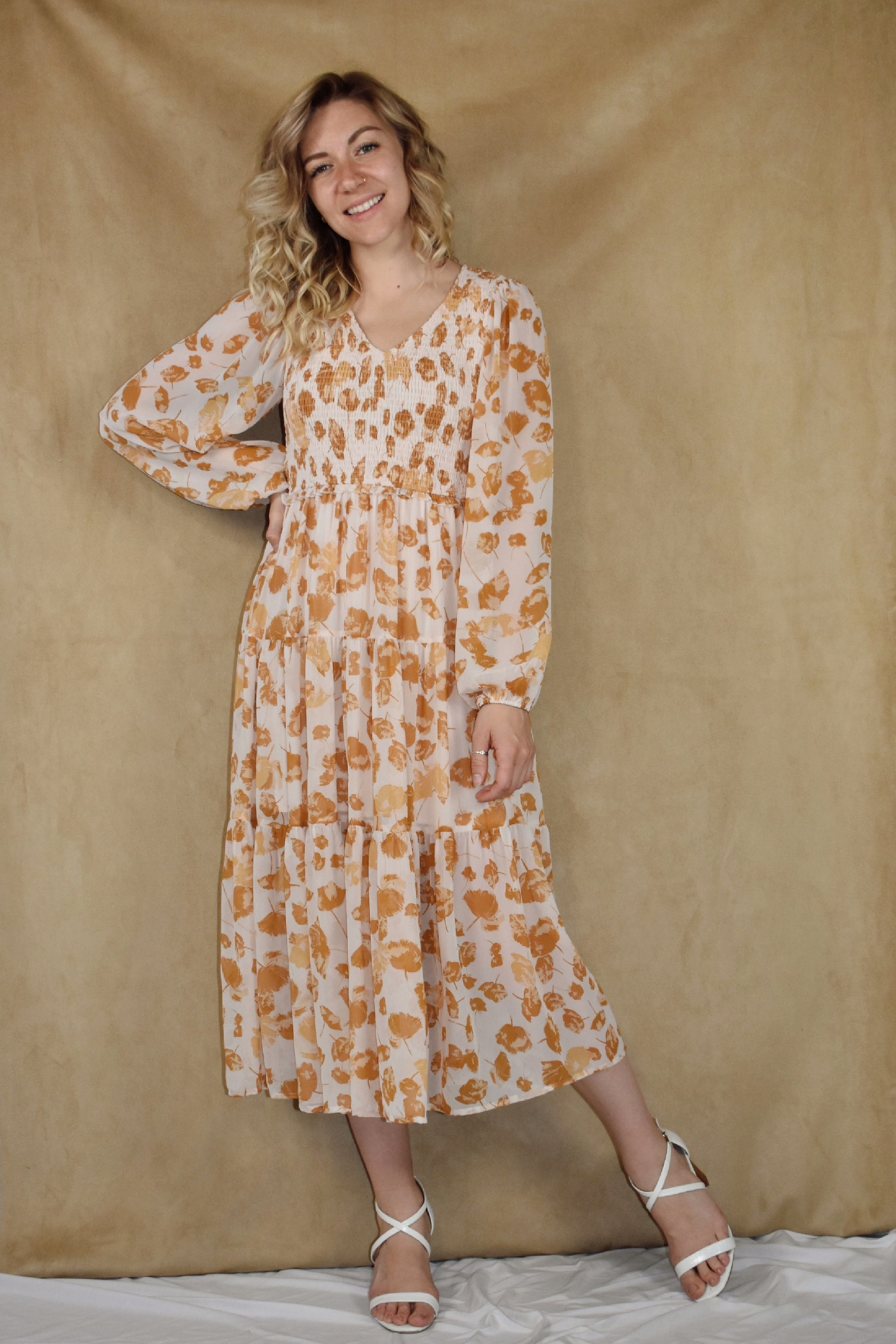 long sleeve midi dress with v neck. printed chiffon fabric infused with flower petals. tiered skirt and smocking detail on bodice. cream and mustard colors.