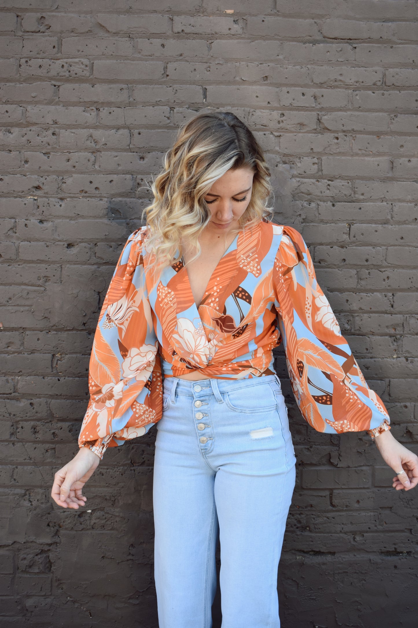light blue and shades of orange printed lightweight long sleeve v neck line top with twist detail in front and smocked cuffs with balloon sleeves. smocked back waistband.