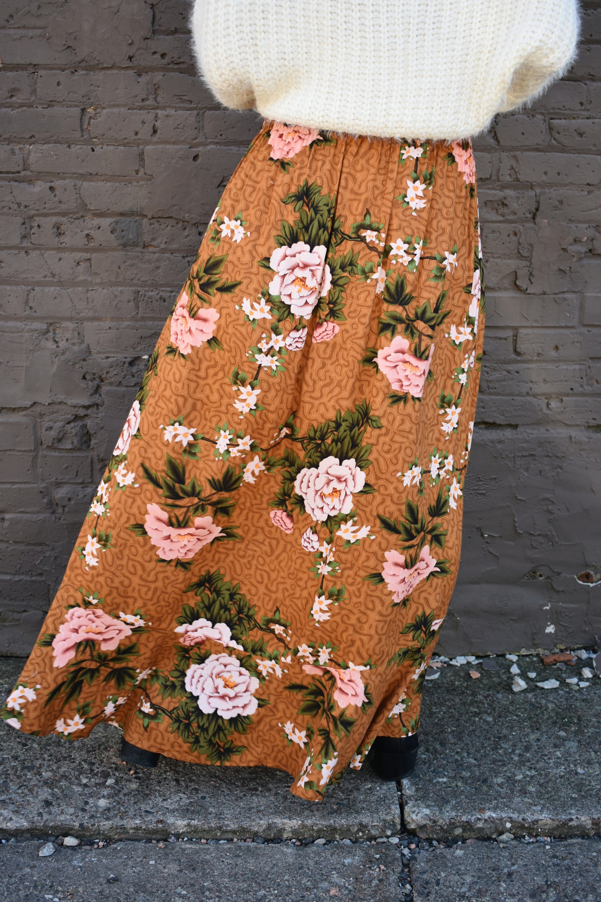 Floral printed maxi skirt with a 3/4 button down front that leads into a center slit. slight ruffle at the bottom. elastic waistband. light brown/rust color background with big printed white and blush colored flowers with green stems.