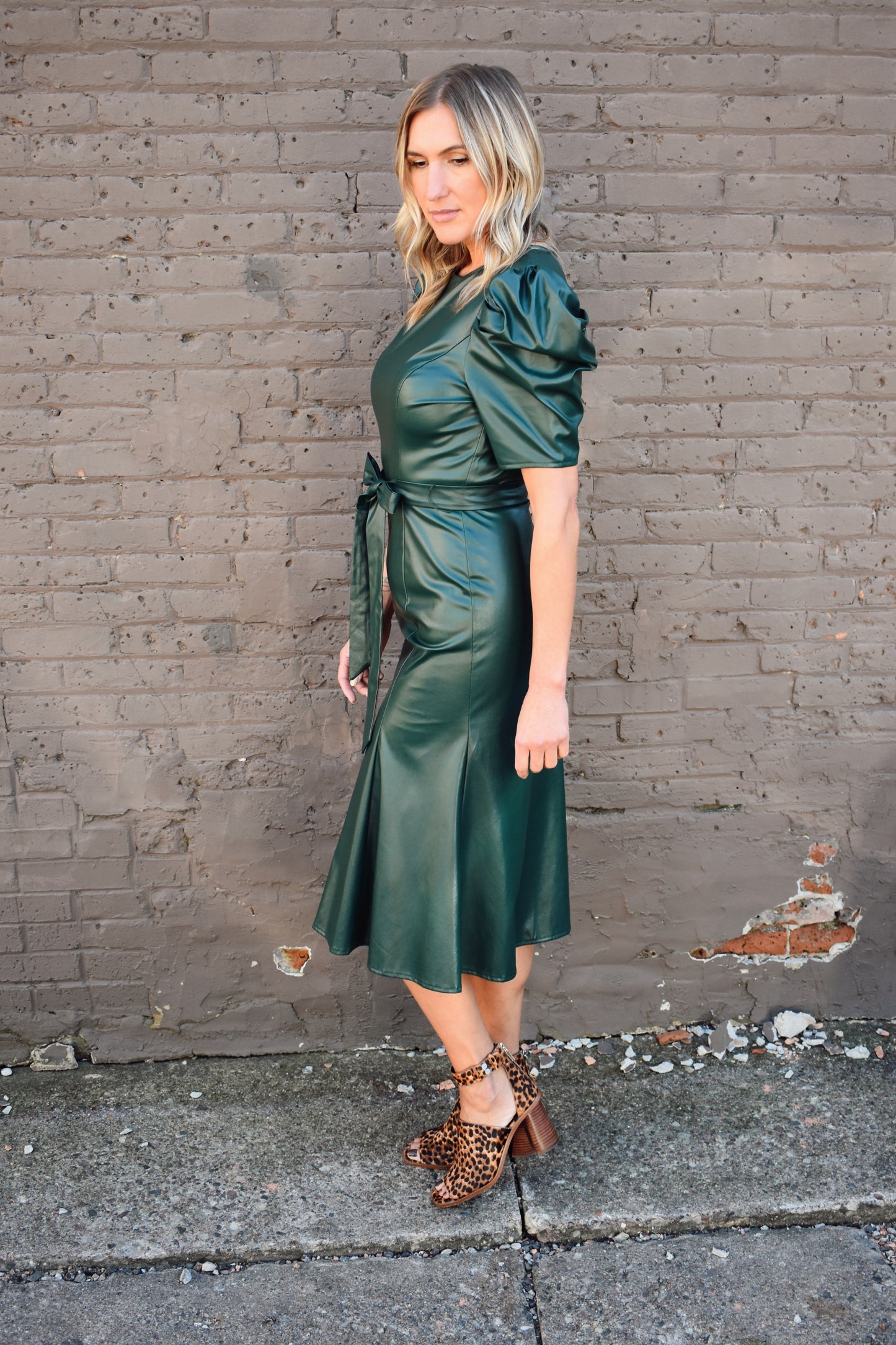 bold dark green faux leather midi dress fitted with slight flare at bottom. Short puff sleeves, crew neck, self tie waist, zipper enclosure