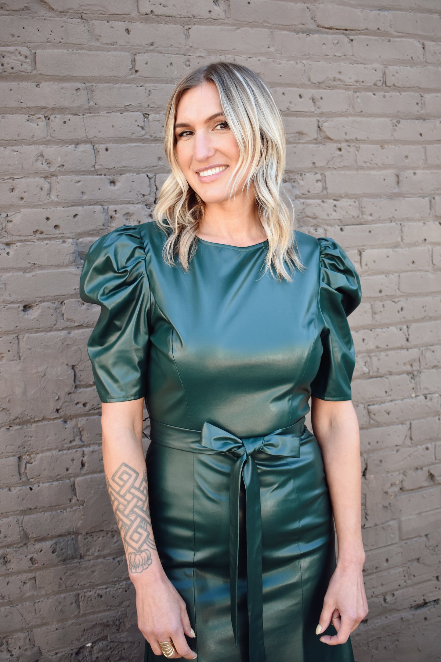 bold dark green faux leather midi dress fitted with slight flare at bottom. Short puff sleeves, crew neck, self tie waist, zipper enclosure