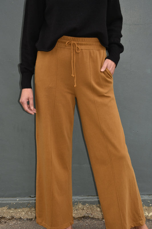 pale brown wide leg athleisure pants with elastic waistband with drawstring, pockets and seam detail down the front of the legs.
