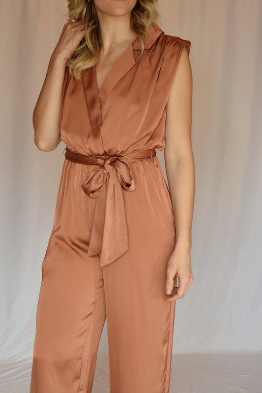 collared v neck sleeveless satin copper toned jumpsuit. Elastic waist with sash tie. front pockets. rushing on top of shoulders.
