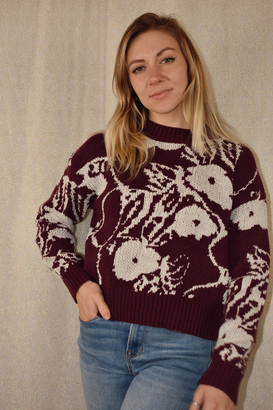 deep purple sweater with white floral pattern. ribbed cuffs hem and neckline. crew neck. waist length